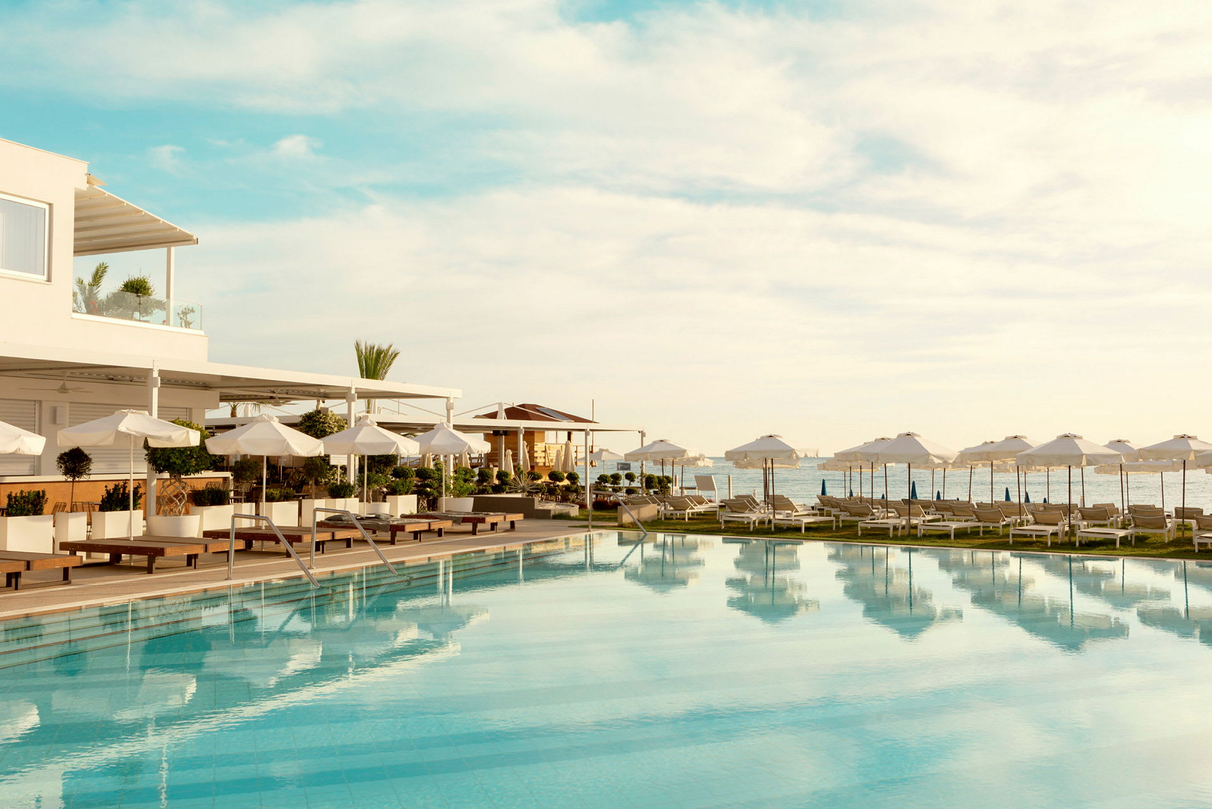 En pool omgiven av solstolar och parasoller vid havet. (AI-genererad text)