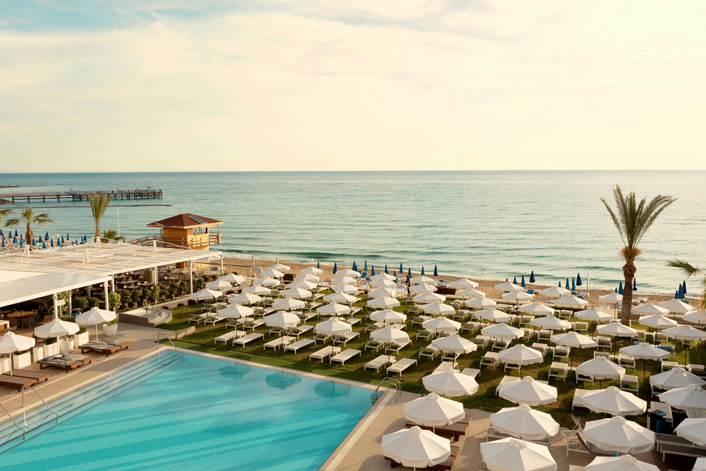 En pool och solstolar med parasoller vid havet. (AI-genererad text)