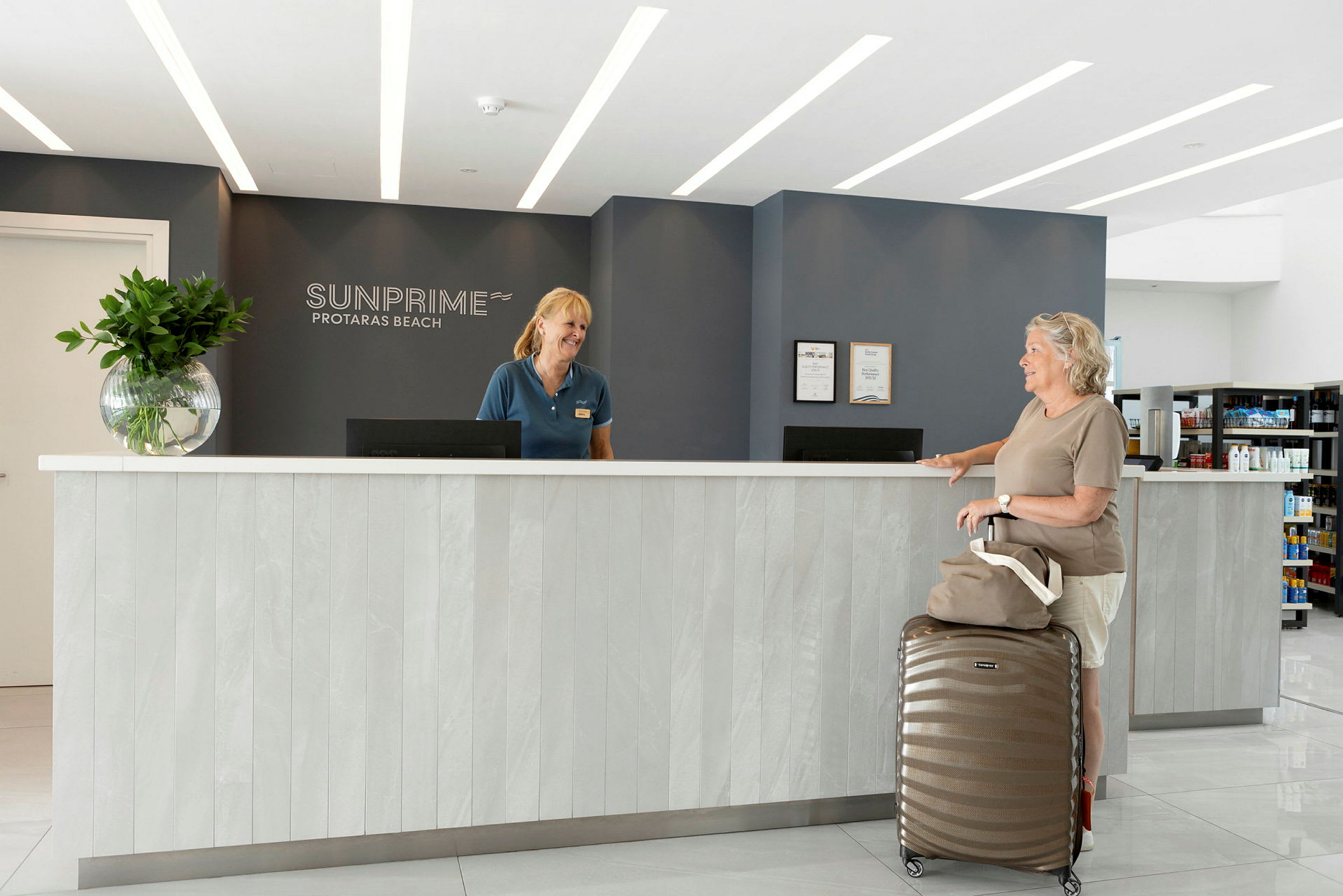 Receptionen på Sunprime Protaras Beach-hotellet med en modern inredning, inkluderande en disk med en resväska och en handväska placerade framför. (AI-genererad text)