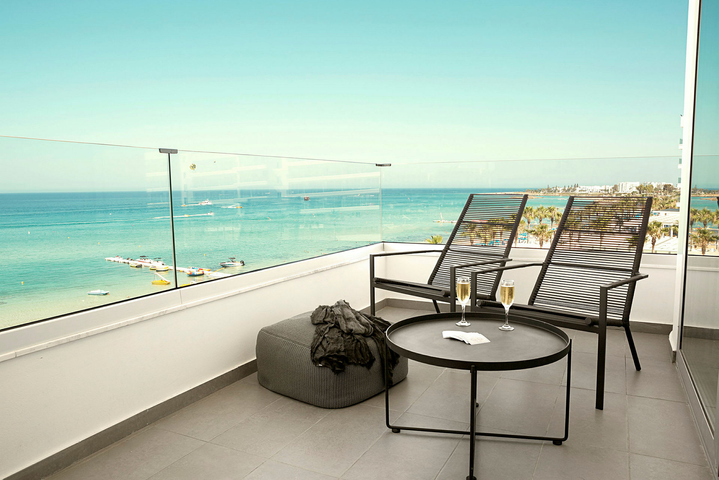Två solstolar och ett bord med två glas står på en terrass med utsikt över havet. (AI-genererad text)