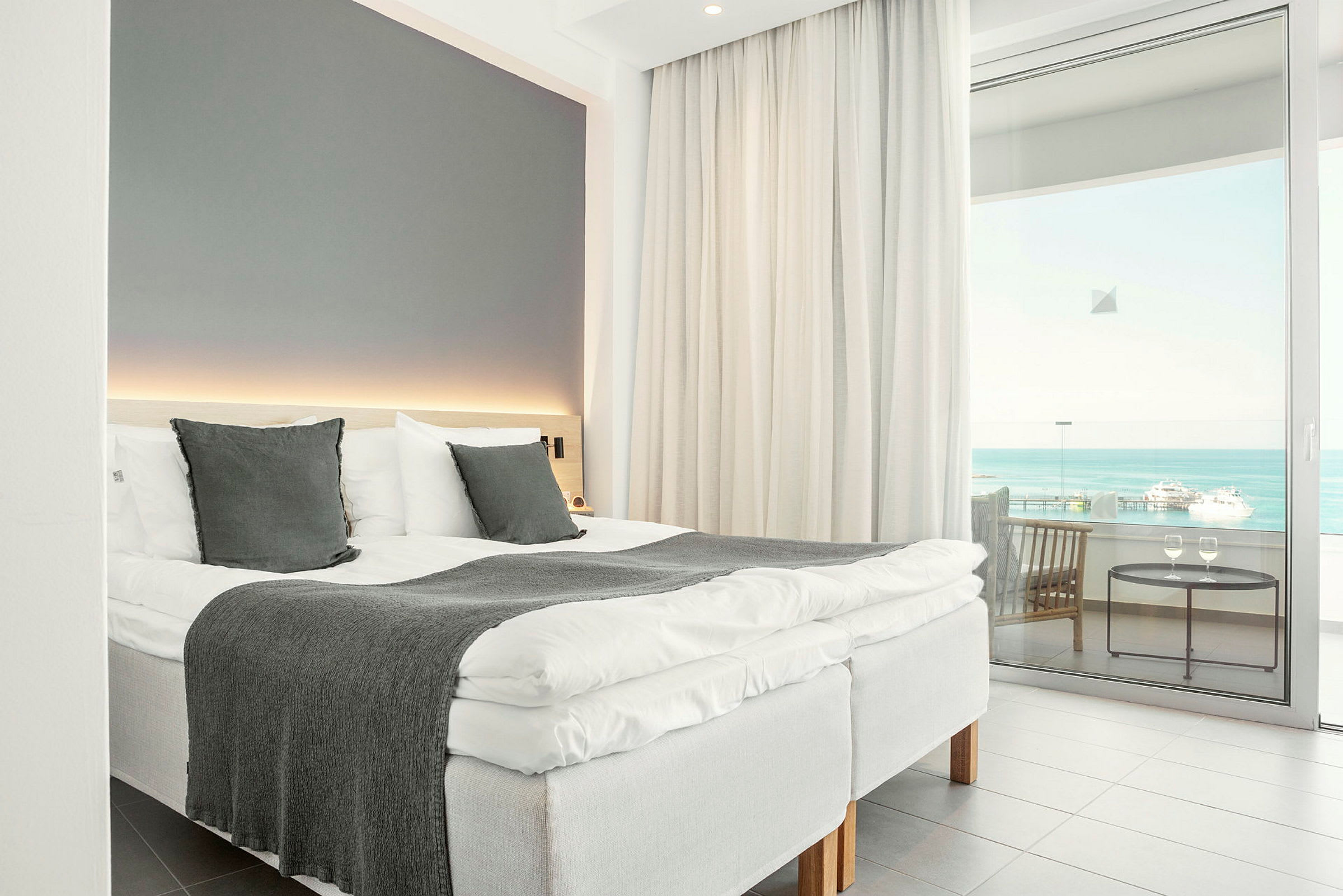 Ett hotellrum med en bäddad säng, stora fönster och utsikt över havet. (AI-genererad text)