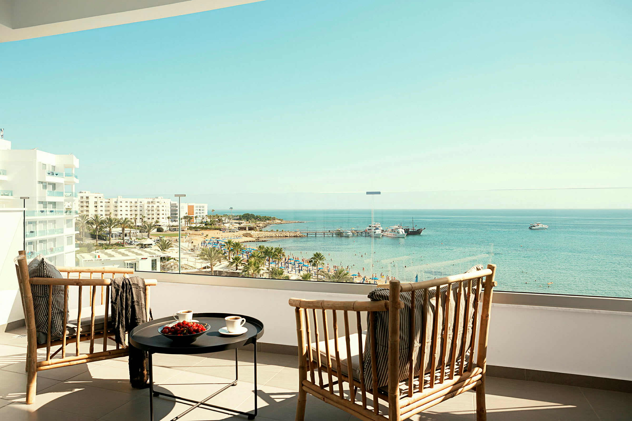 Två trästolar och ett bord på ett hotellbalkong med utsikt över strand och hav. (AI-genererad text)