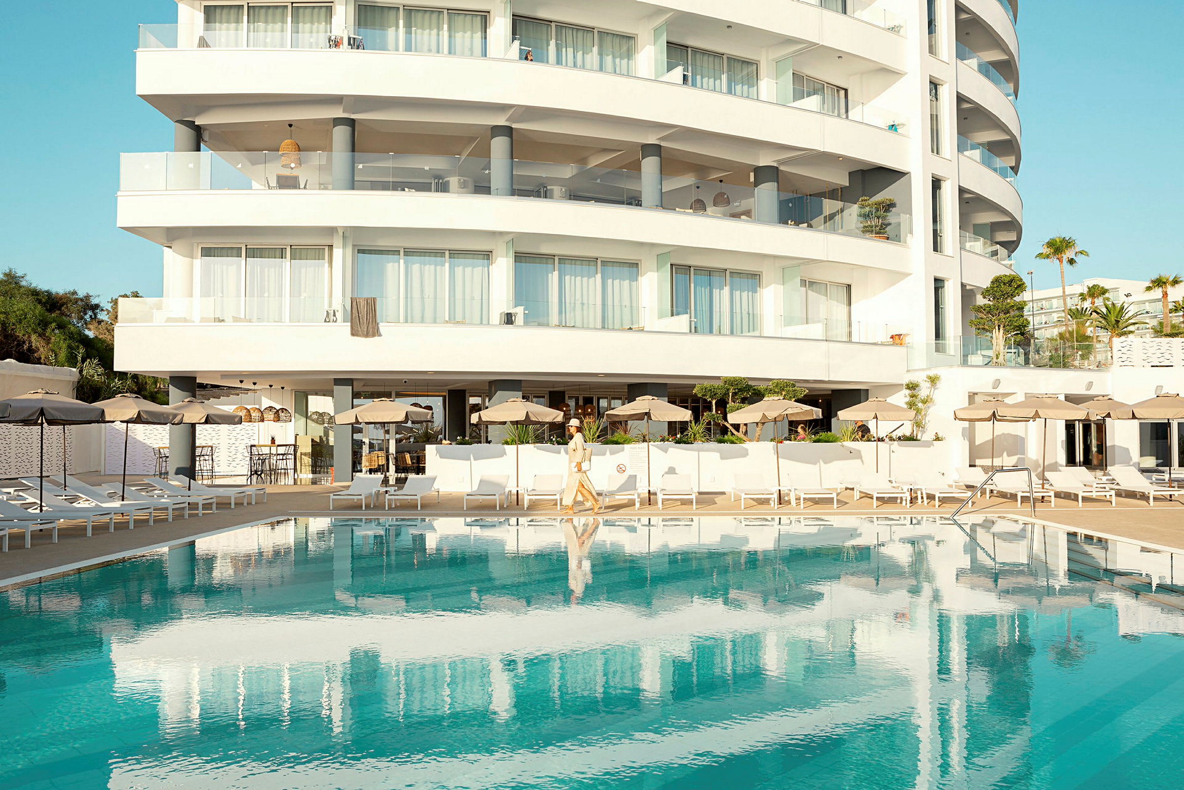 Vit byggnad med balkonger och en pool framför. (AI-genererad text)