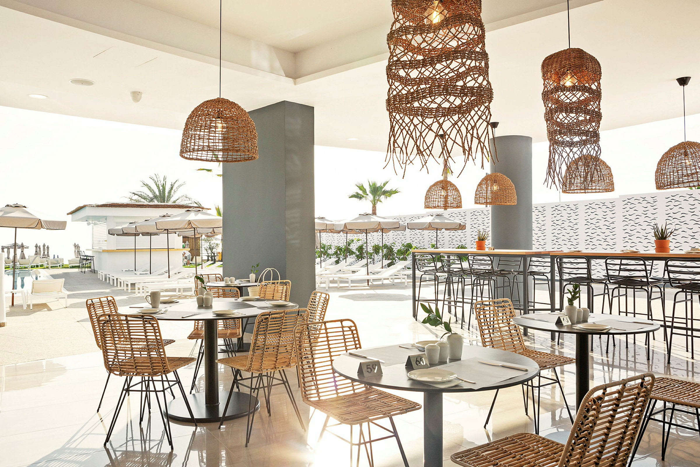 En restaurang med rottingmöbler och dekorationer med utsikt över en pool och solstolar. (AI-genererad text)