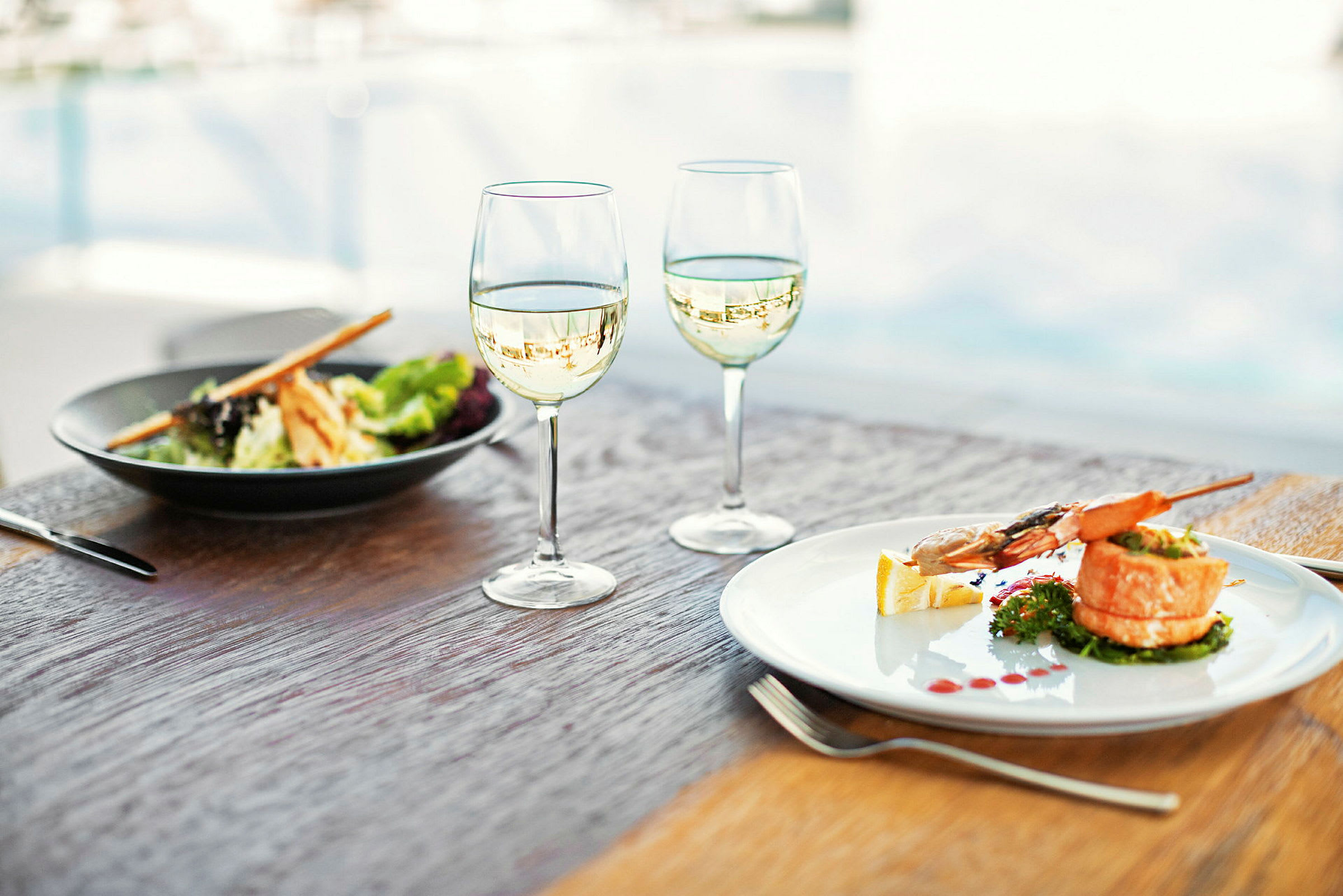 Två vinglas samt en tallrik med seafood på ett bord. (AI-genererad text)