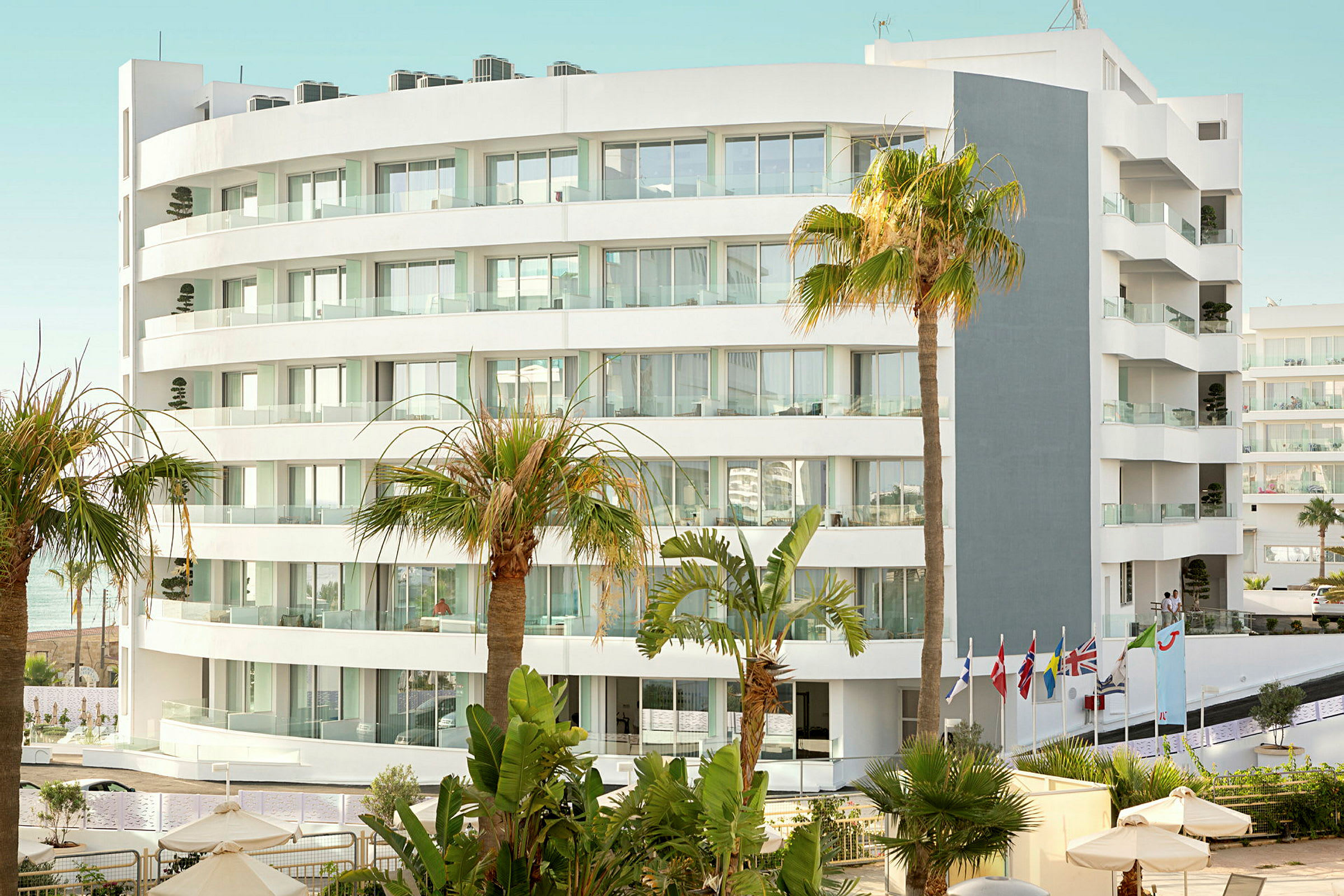 Bild av en modern vit hotellbyggnad omgiven av palmer och vegetation. (AI-genererad text)