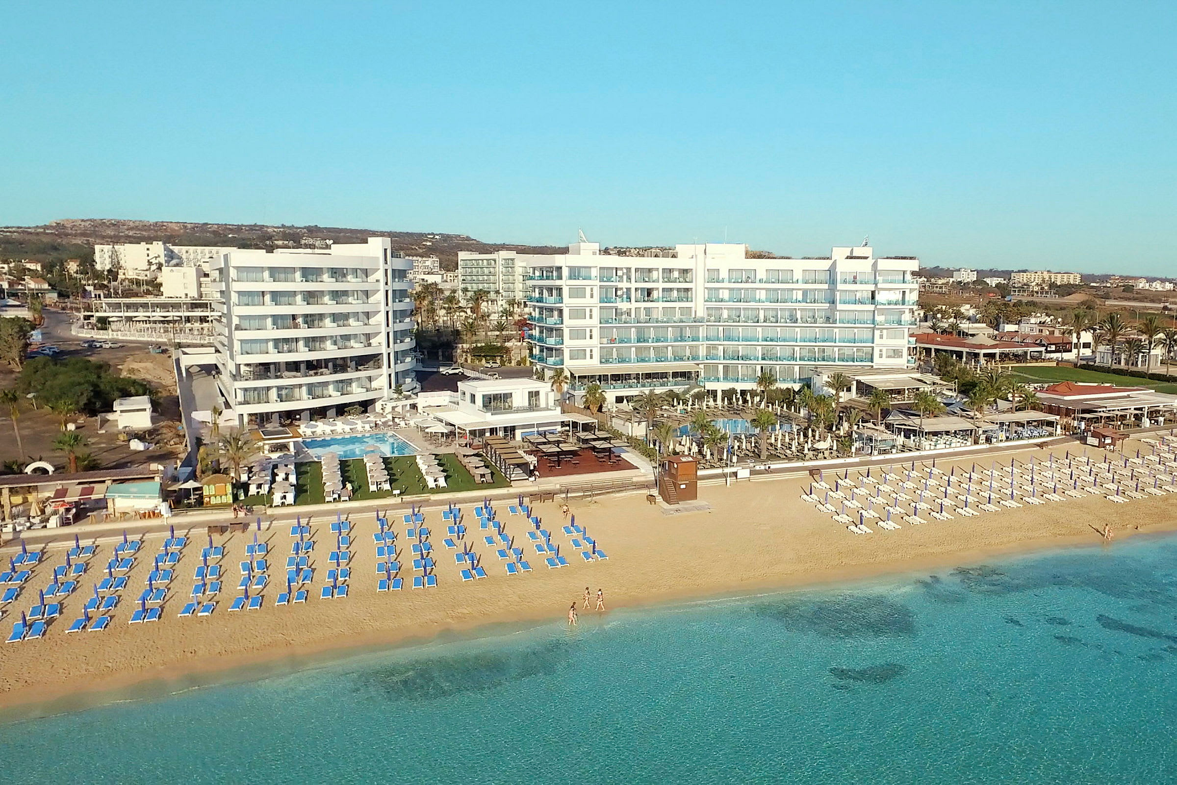 Bild av en strand med solstolar och parasoller framför ett hotell vid kusten. (AI-genererad text)