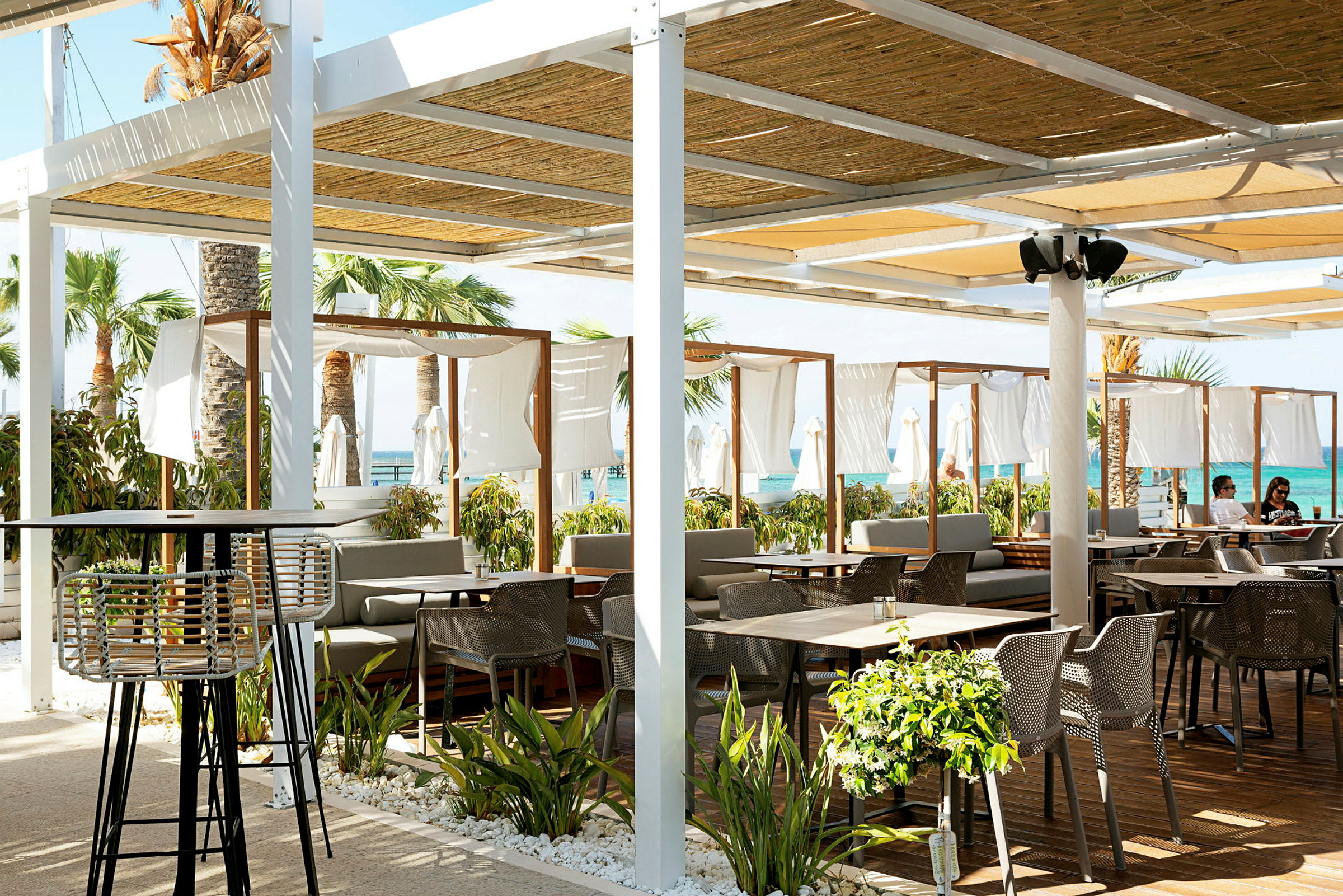 Strandnära restaurang med utomhusmöbler och dekorerande växtlighet. (AI-genererad text)