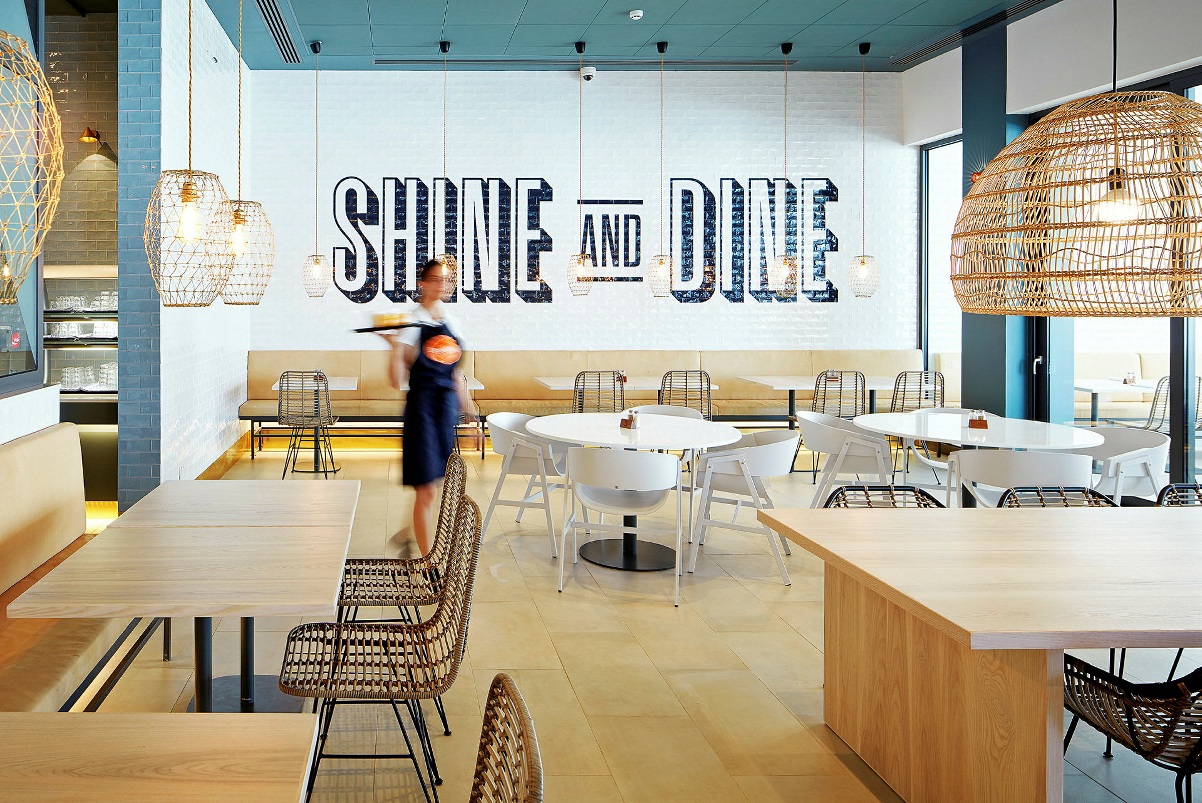 En modern restaurang med sittplatser, belysning och text på väggen som säger 'Shine and Dine'. (AI-genererad text)