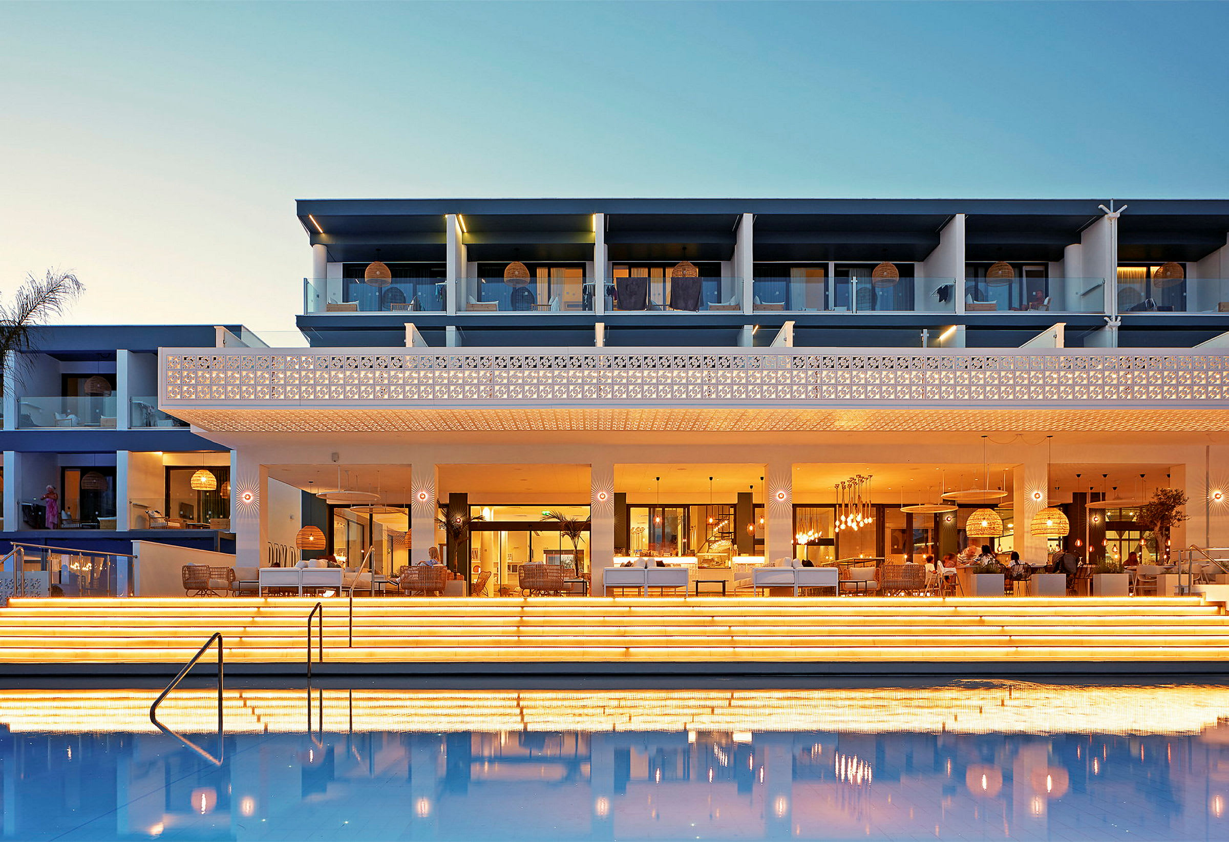 Hotellfasad med upplysta trappor och en pool i förgrunden på kvällen. (AI-genererad text)