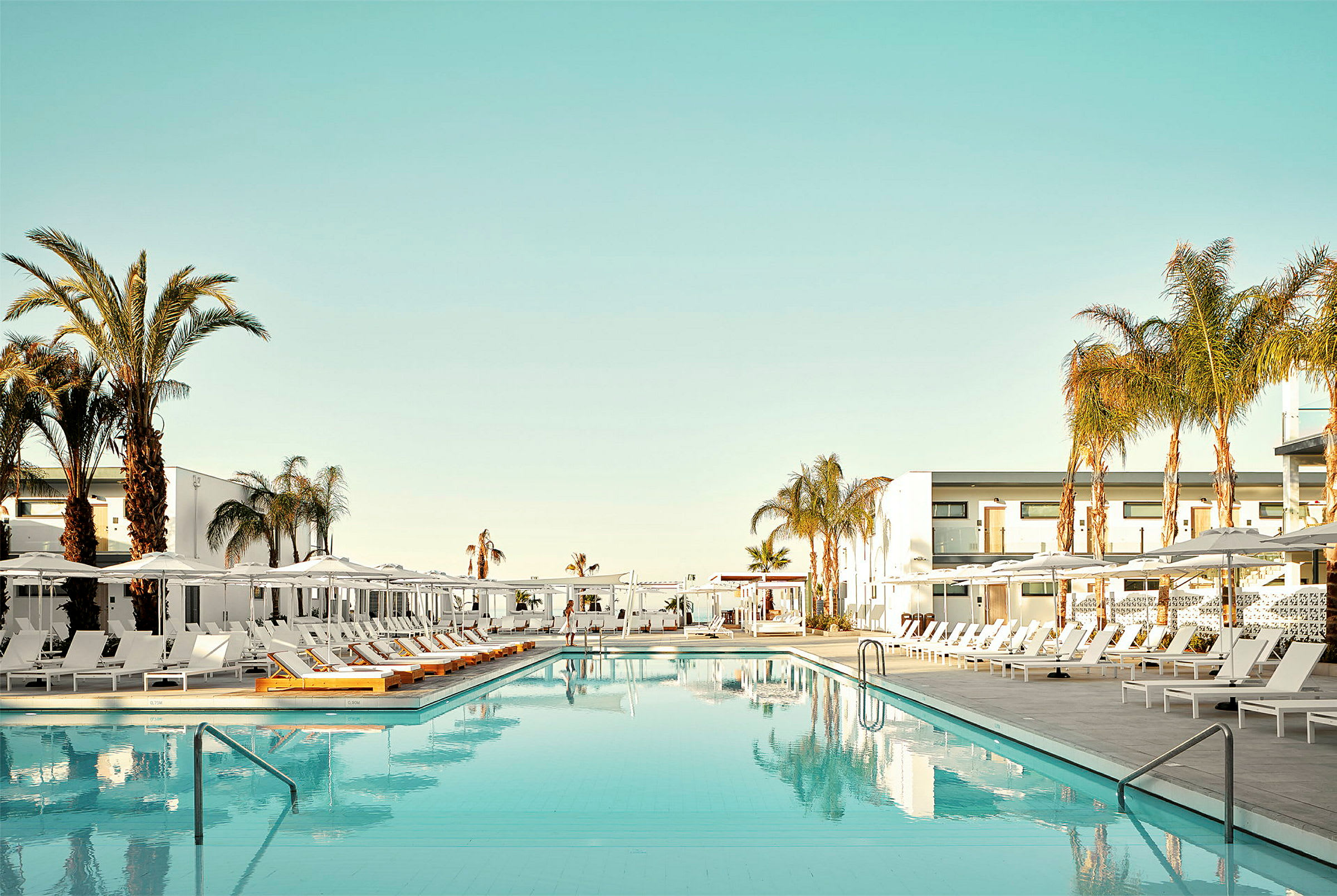 En swimmingpool omgiven av solstolar och palmer vid ett hotell. (AI-genererad text)