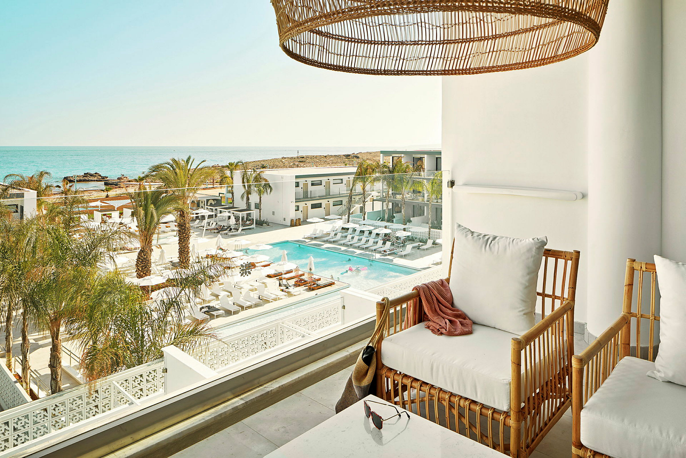 En terrass med sittmöbler med utsikt över en pool och havet i bakgrunden. (AI-genererad text)