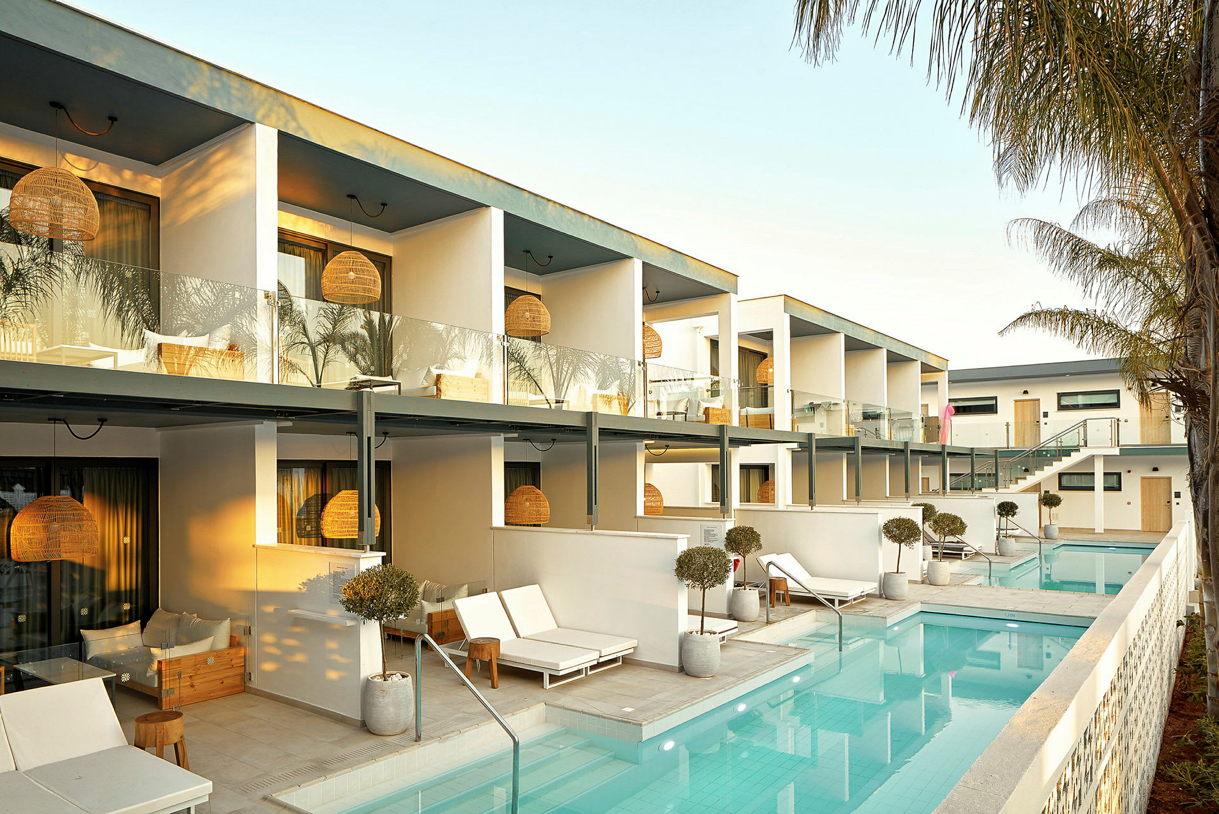 Hotellfoto med pool och solstolar framför moderna byggnader. (AI-genererad text)