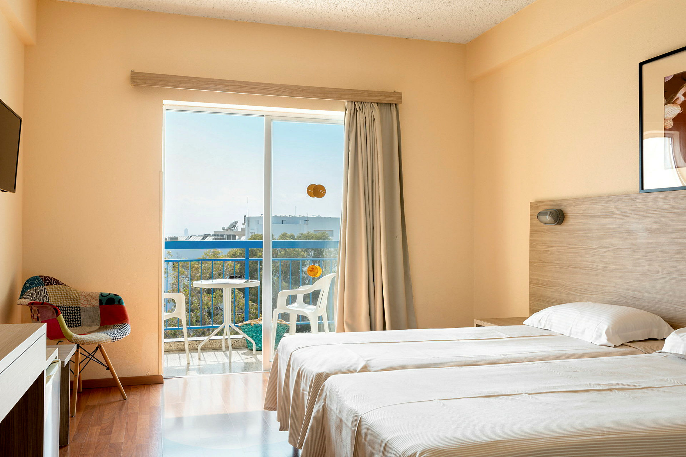 Ett hotellrum med två enkelsängar, en stol, TV, samt en balkong med utsikt. (AI-genererad text)