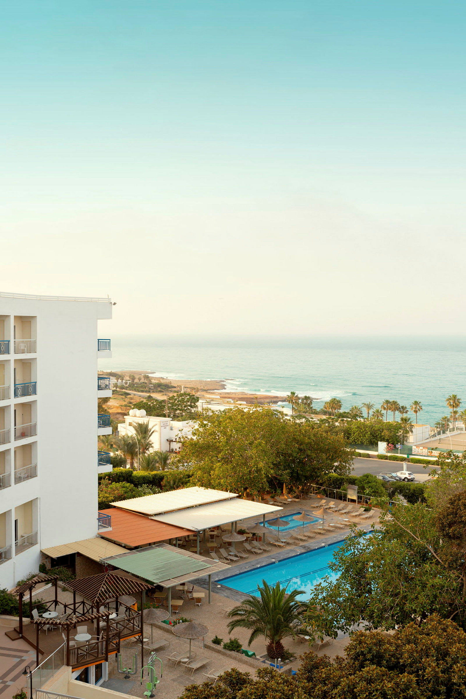 En hotellbyggnad vid kusten med poolområde med solstolar och parasoller. (AI-genererad text)