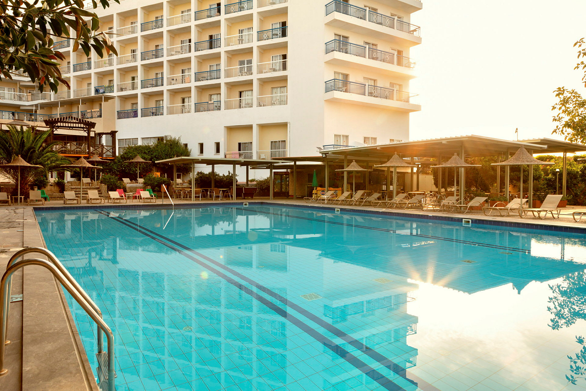 Utomhuspool vid ett hotell med solstolar och parasoller runtom. (AI-genererad text)