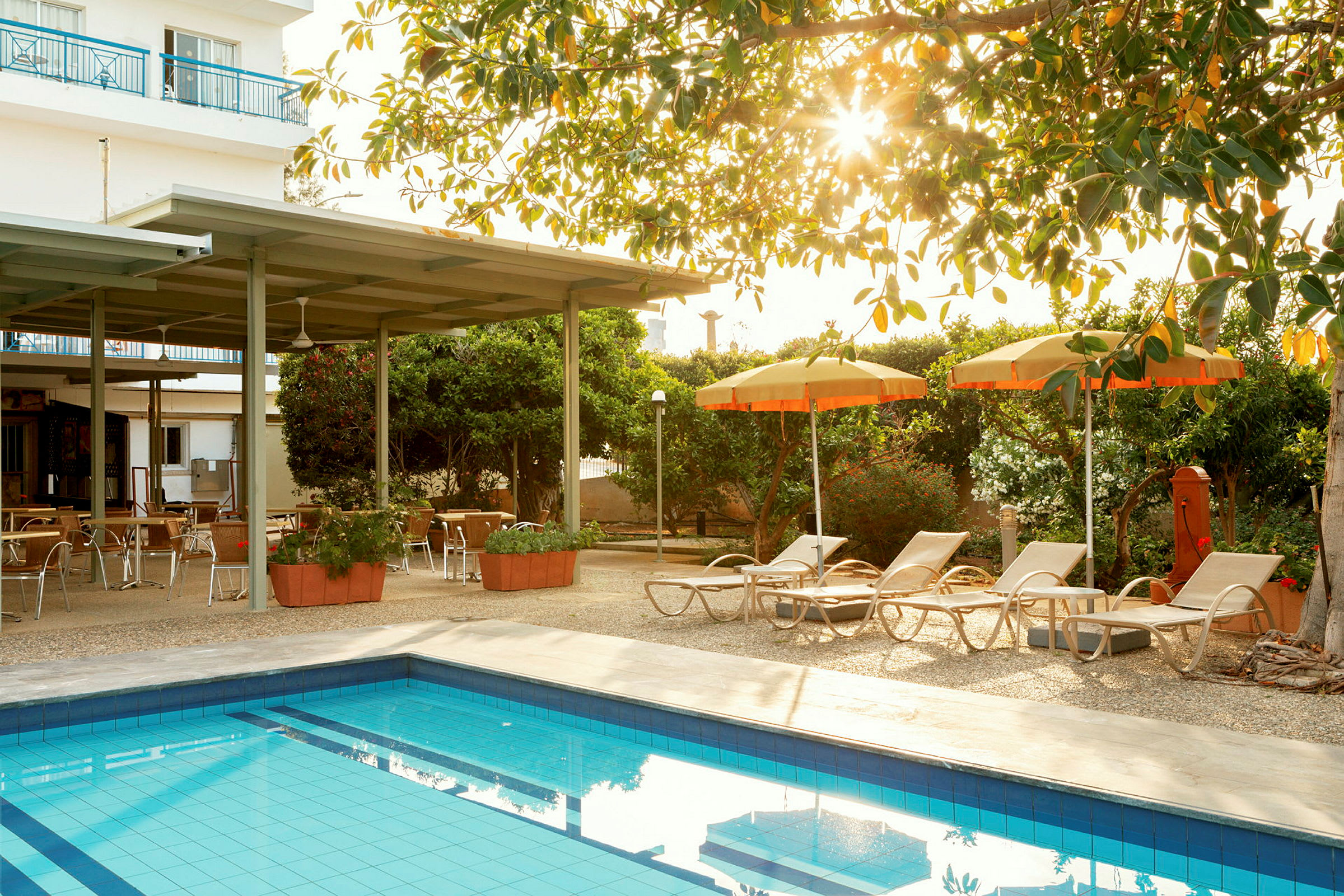 Utomhusområde med en pool, solsängar och parasoller, samt sittplatser under en pergola. (AI-genererad text)