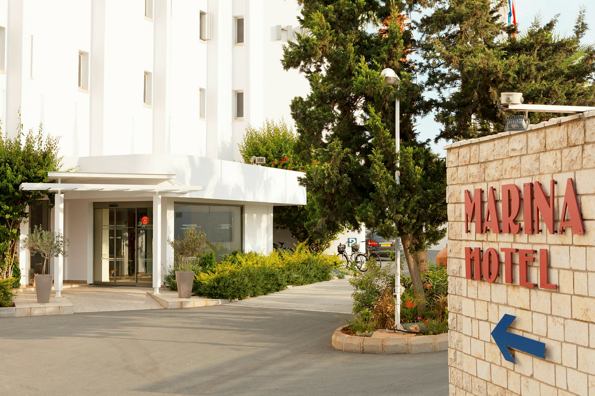 Entré till Marina Hotel med gröna växter och skylt. (AI-genererad text)