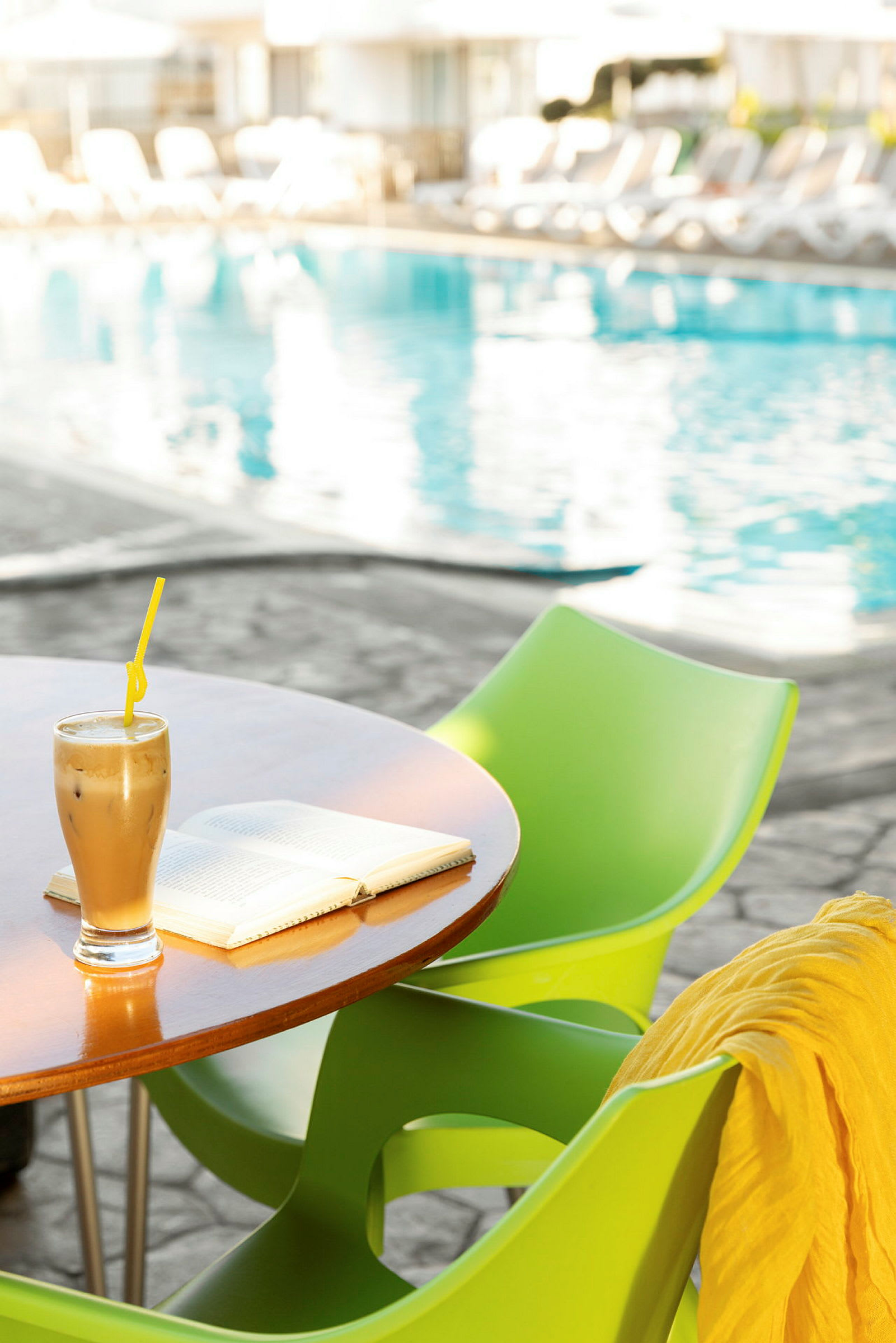 Ett bord med en kaffedryck och en bok, bredvid en pool. (AI-genererad text)
