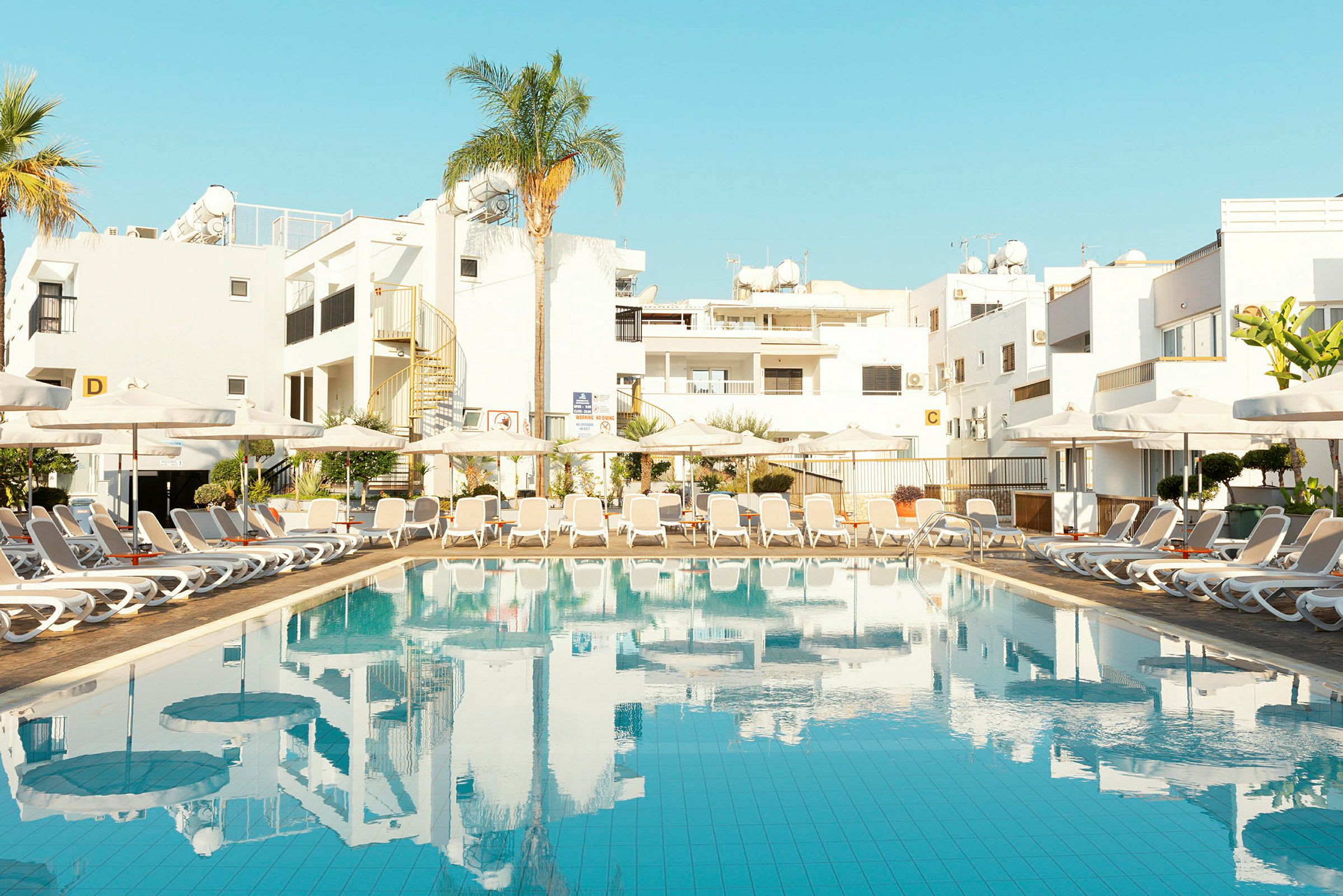 Pool med solstolar och byggnader i bakgrunden. (AI-genererad text)