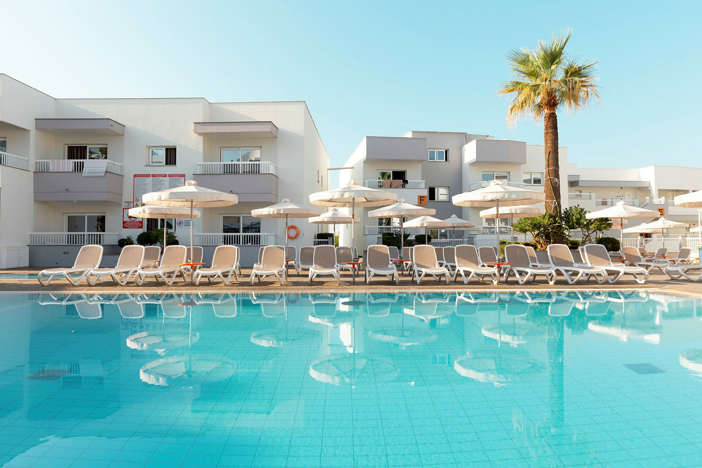 Bild av en pool med solstolar och parasoller framför ett hotell. (AI-genererad text)