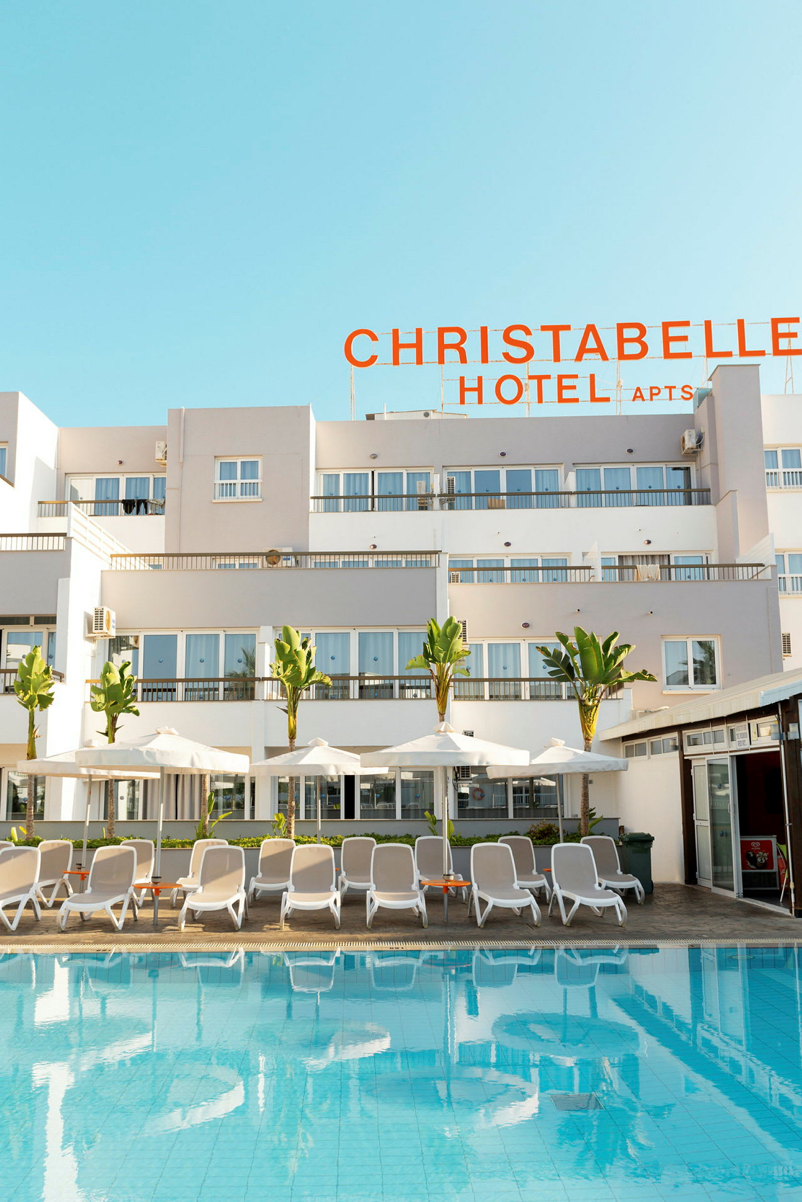 Utomhuspool med solstolar och parasoller framför Christabelle Hotel. (AI-genererad text)