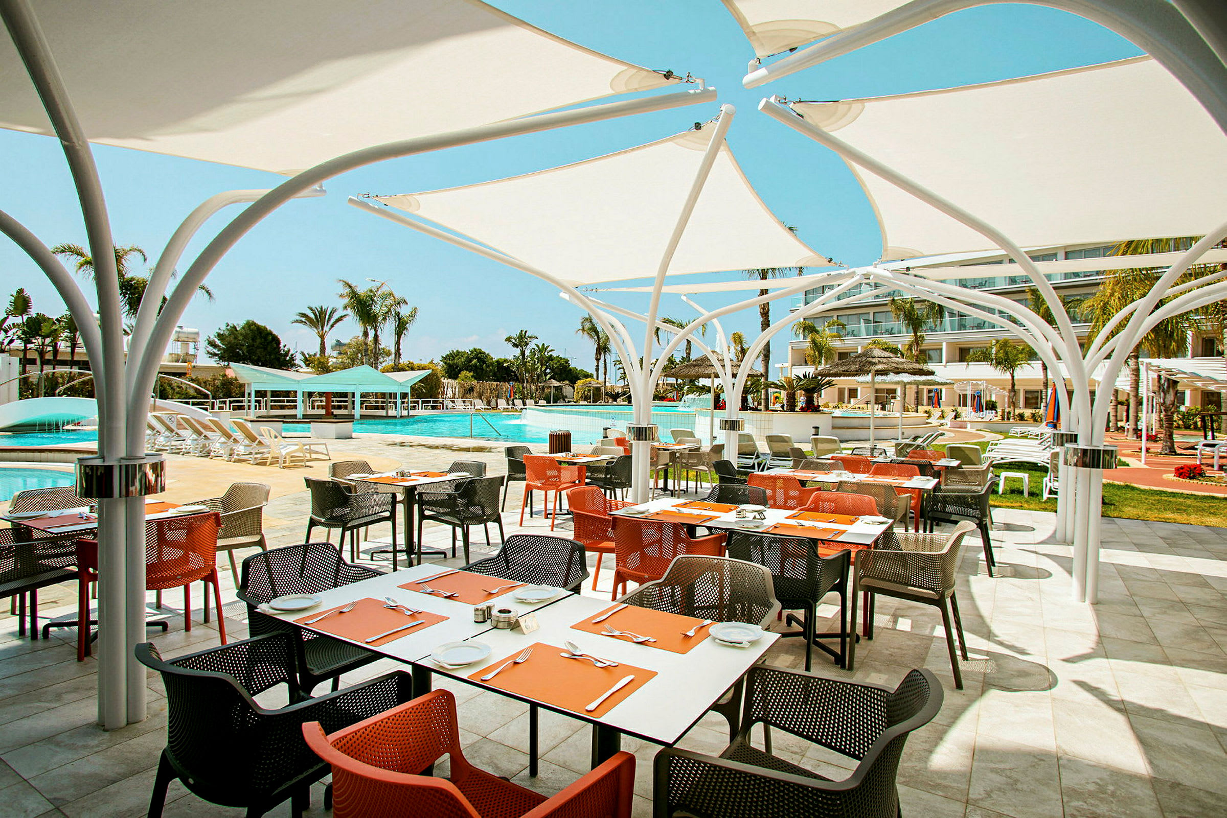 Utomhusrestaurang med färgglada stolar och bord nära en pool. (AI-genererad text)