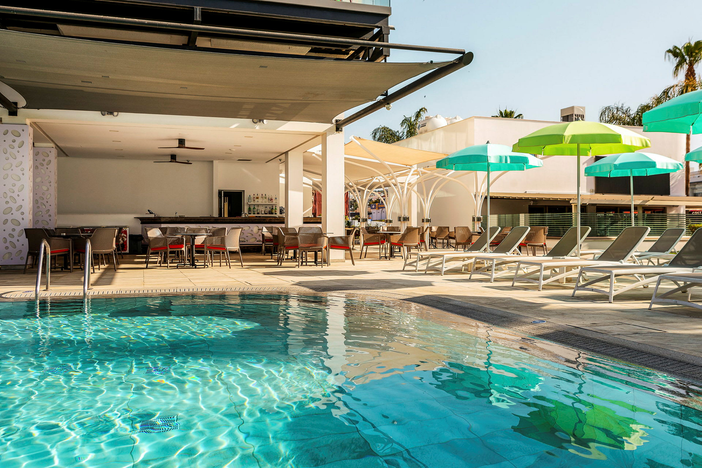 Poolområde med solsängar och parasoller samt en bar i bakgrunden. (AI-genererad text)