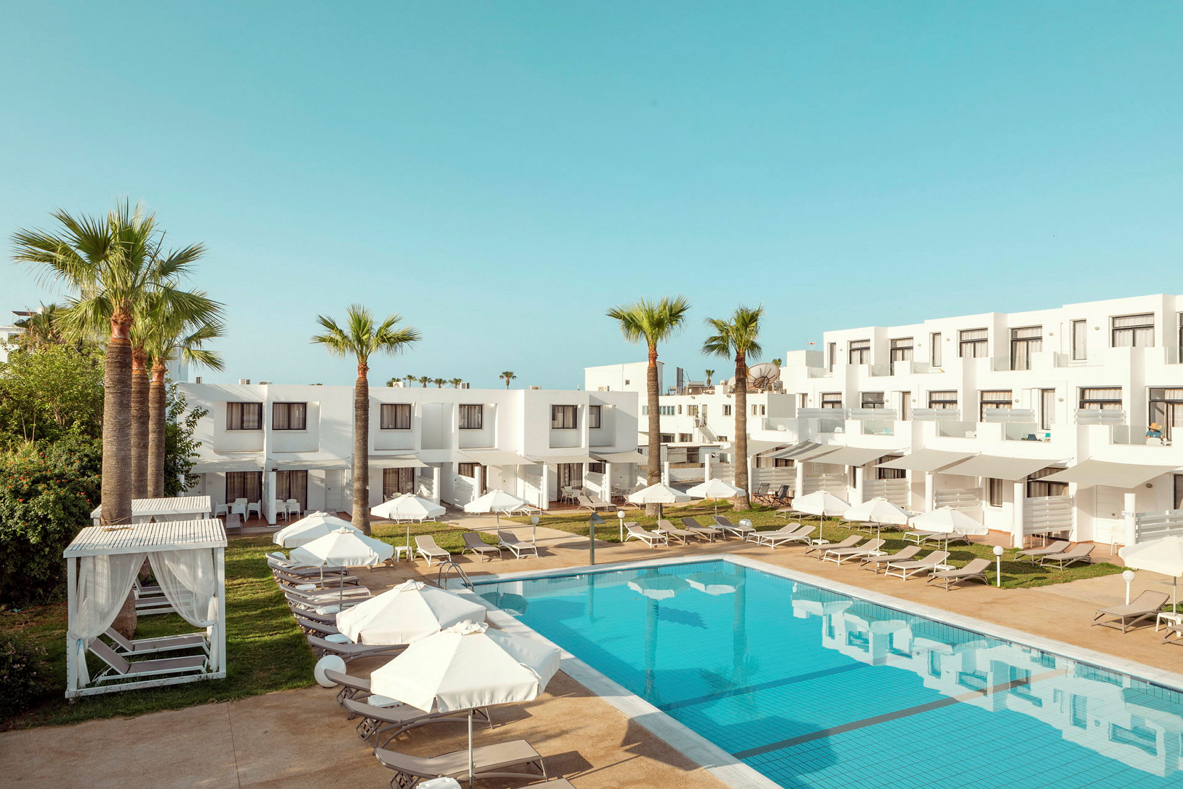 Hotellområde med pool och vita byggnader, omgiven av palmer och solstolar. (AI-genererad text)