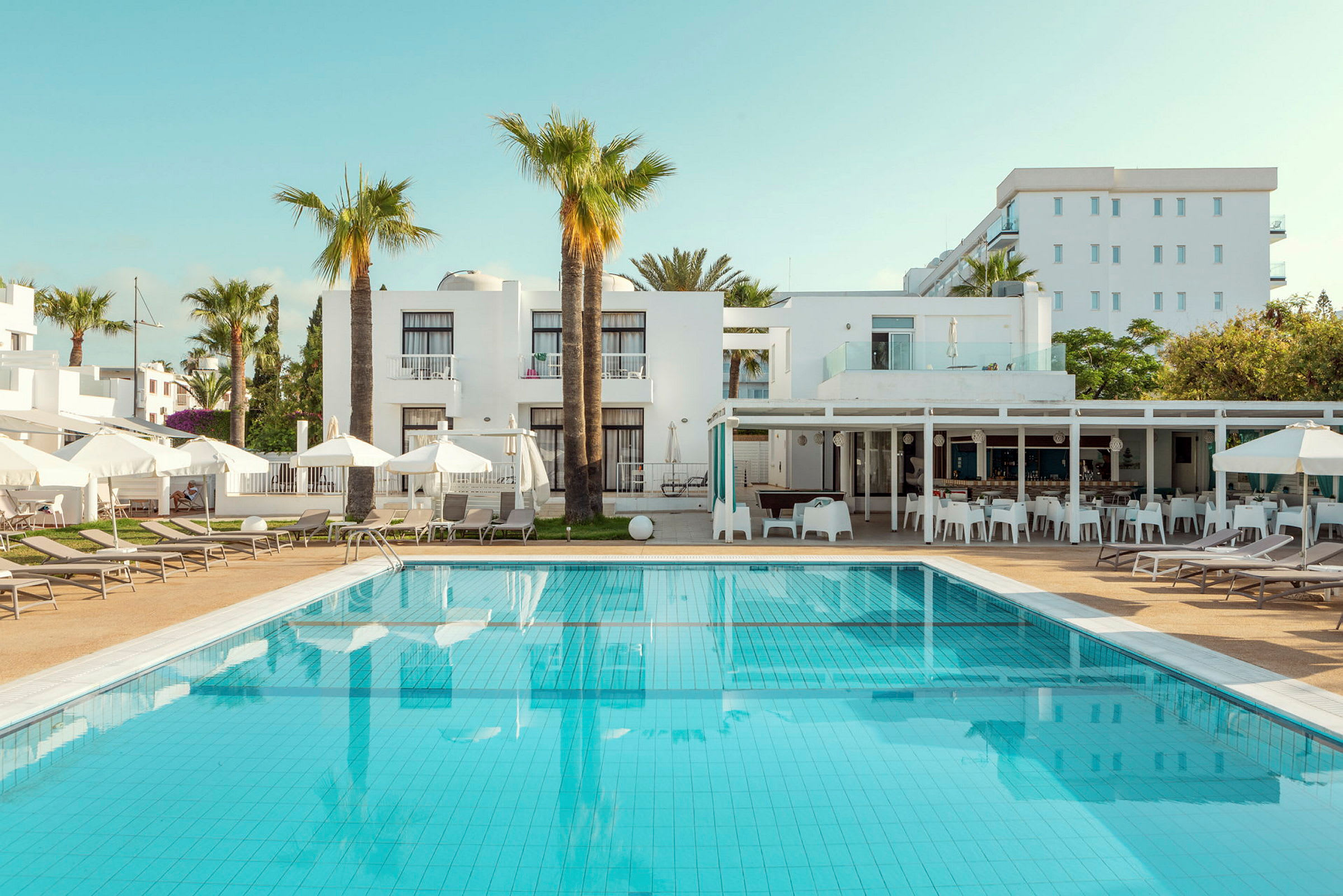 Bild av hotellpool med solstolar och vita byggnader i bakgrunden. (AI-genererad text)