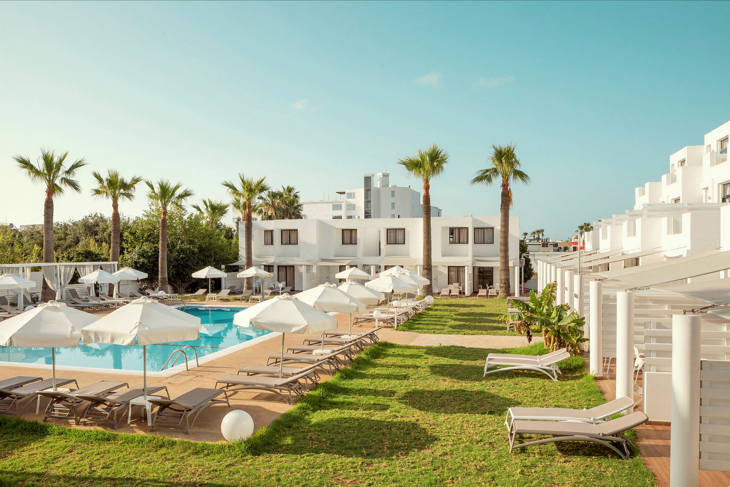 Poolområde vid hotell med solstolar och parasoller, omgiven av palmer och gräs. (AI-genererad text)