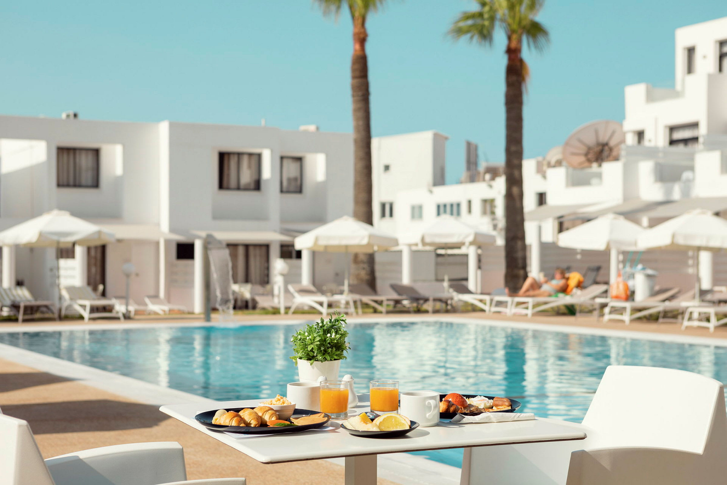En frukost serverad vid ett bord med utsikt över en pool och solstolar. (AI-genererad text)