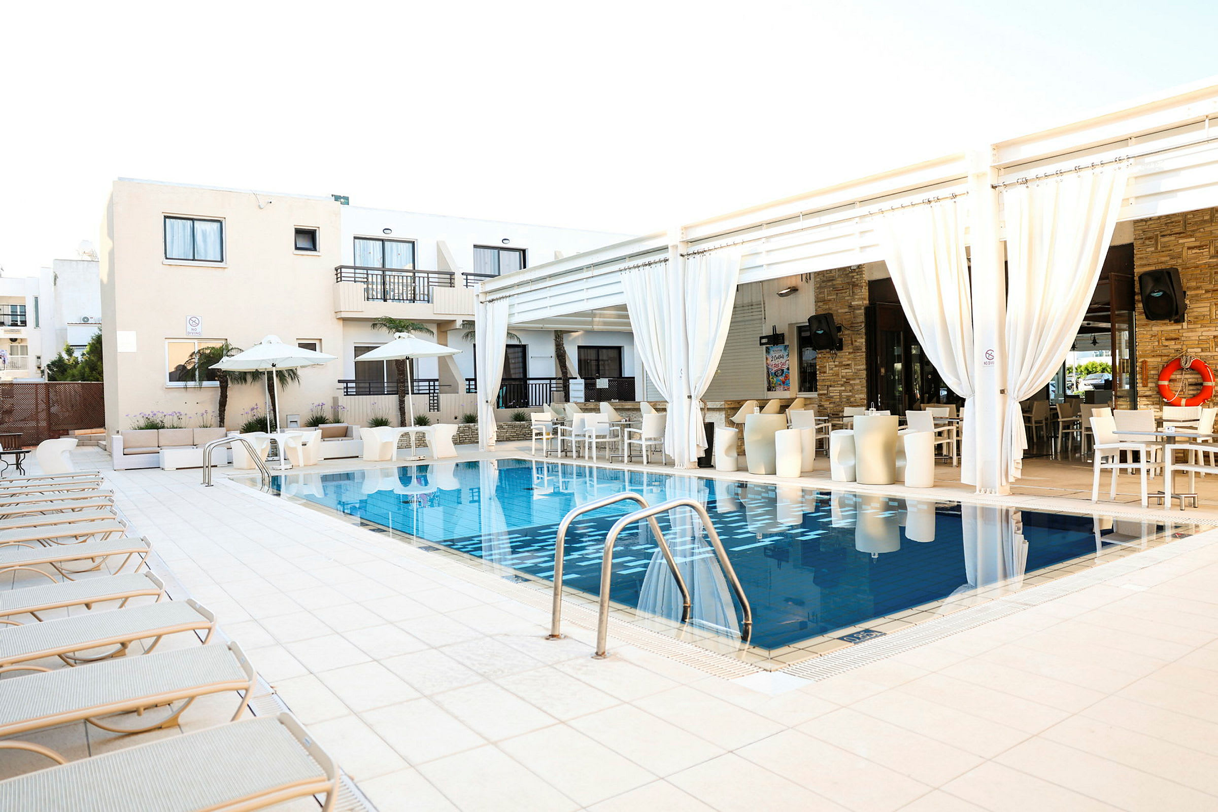 Ett hotellområde med en pool omgiven av solstolar och vita byggnader med balkonger. (AI-genererad text)