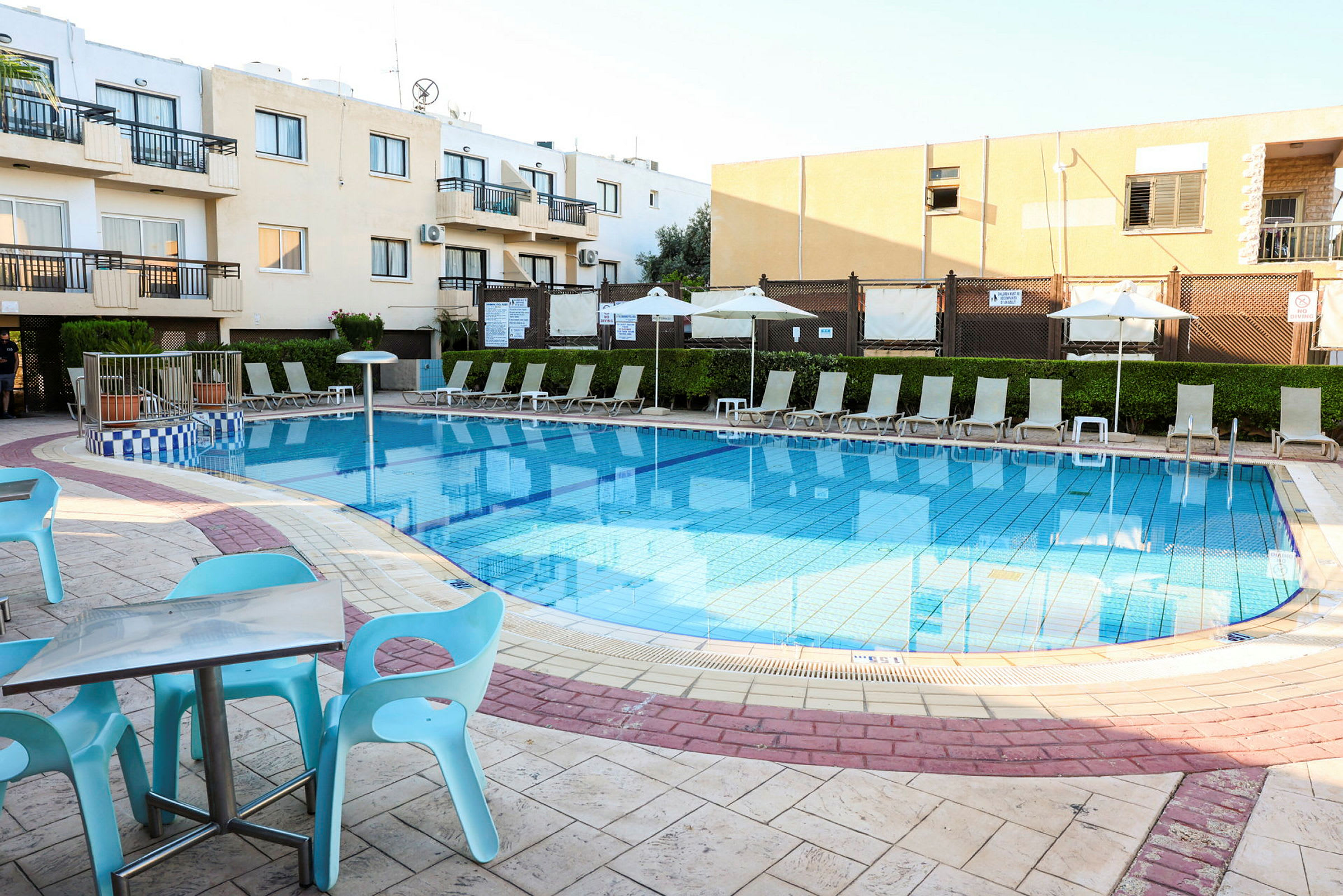 En pool med omkringliggande solstolar och parasoller vid en hotellkomplex. (AI-genererad text)