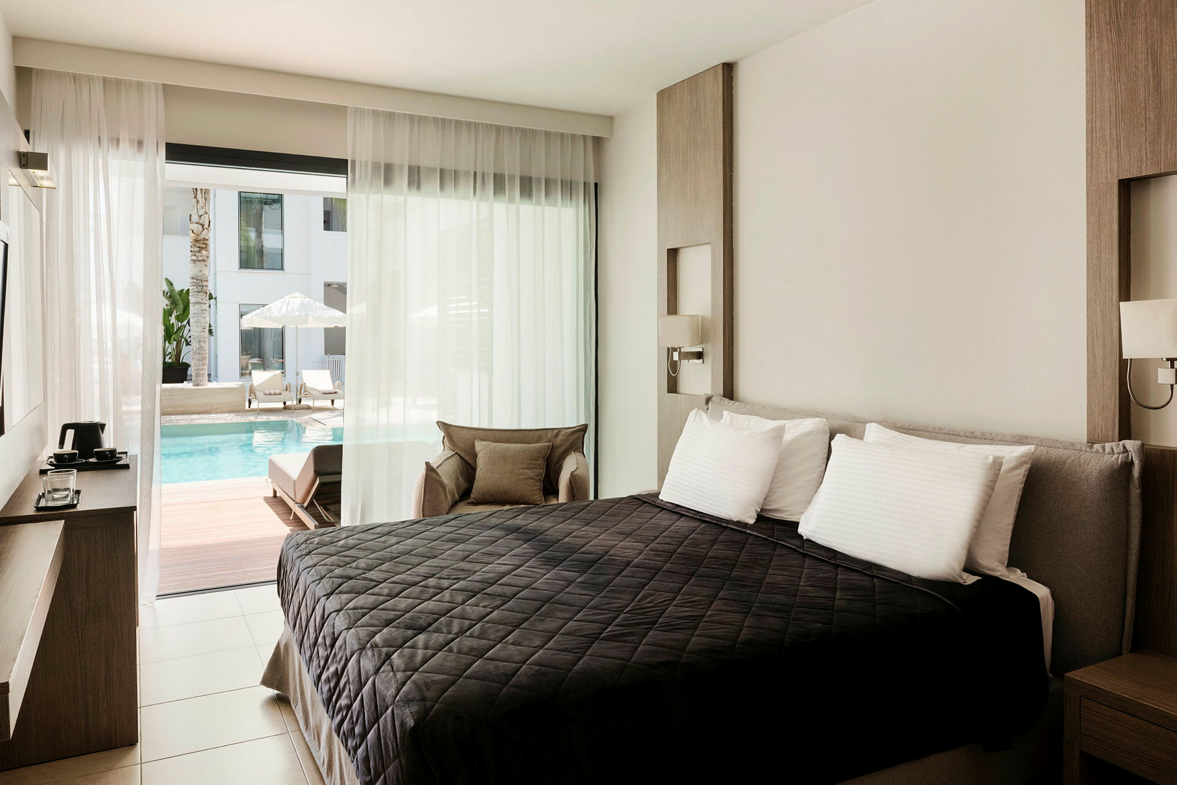 Ett hotellrum med en säng framför en skjutdörr som leder till en uteplats vid en pool. (AI-genererad text)