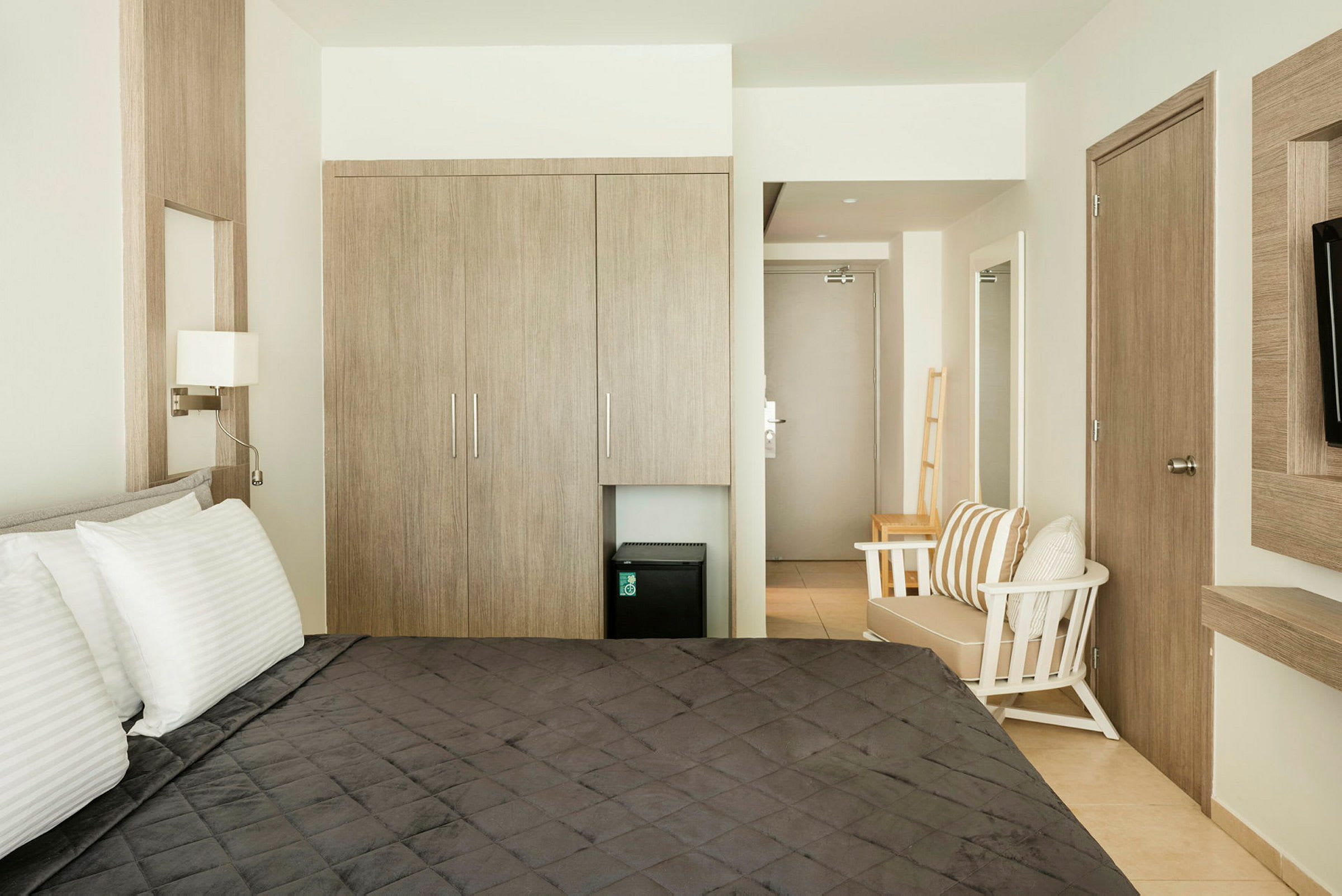 Ett hotellrum med en säng, garderob, stol och en liten kyl under garderoben. (AI-genererad text)