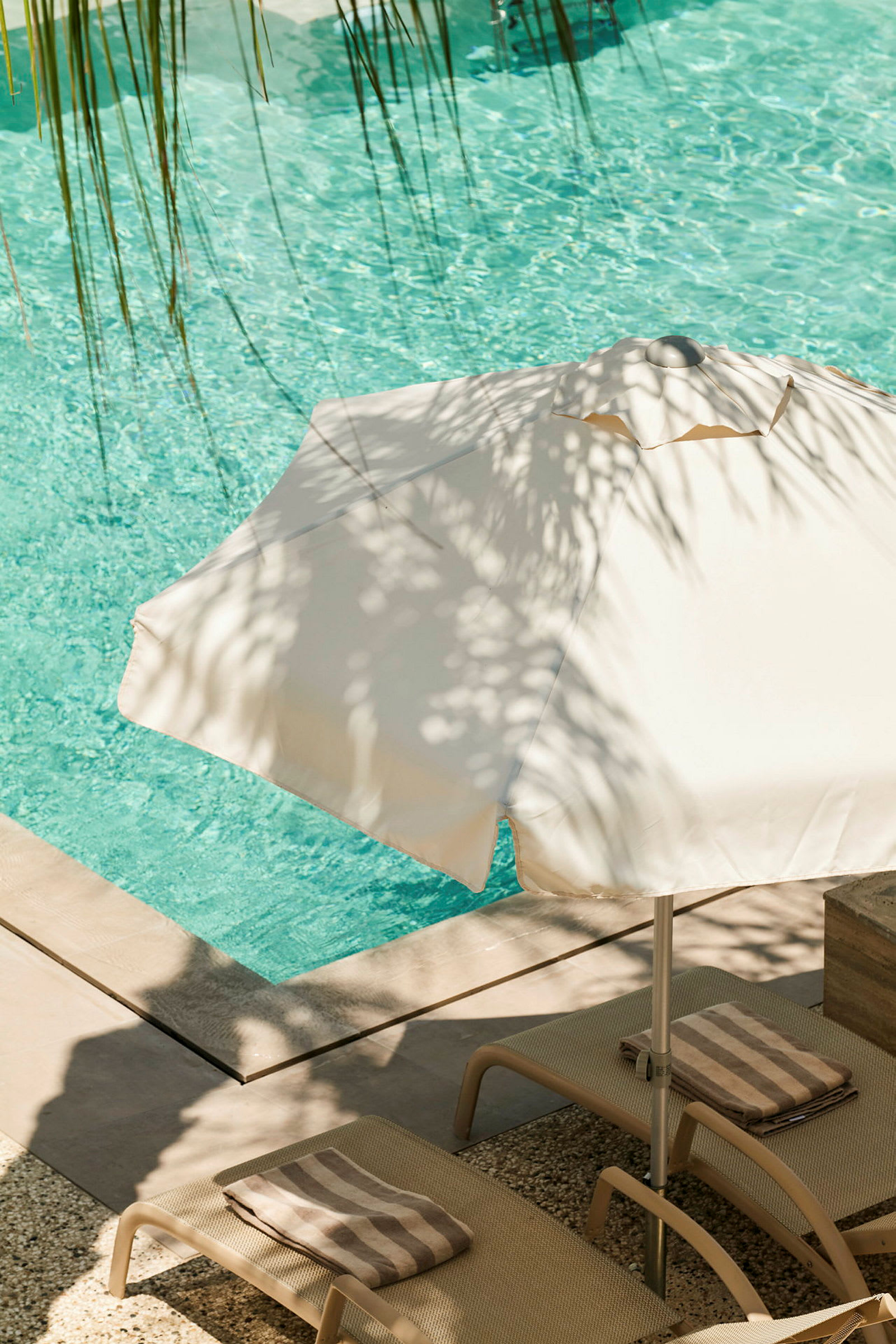 Ett parasoll står brevid två solstolar och en pool med klart vatten. (AI-genererad text)