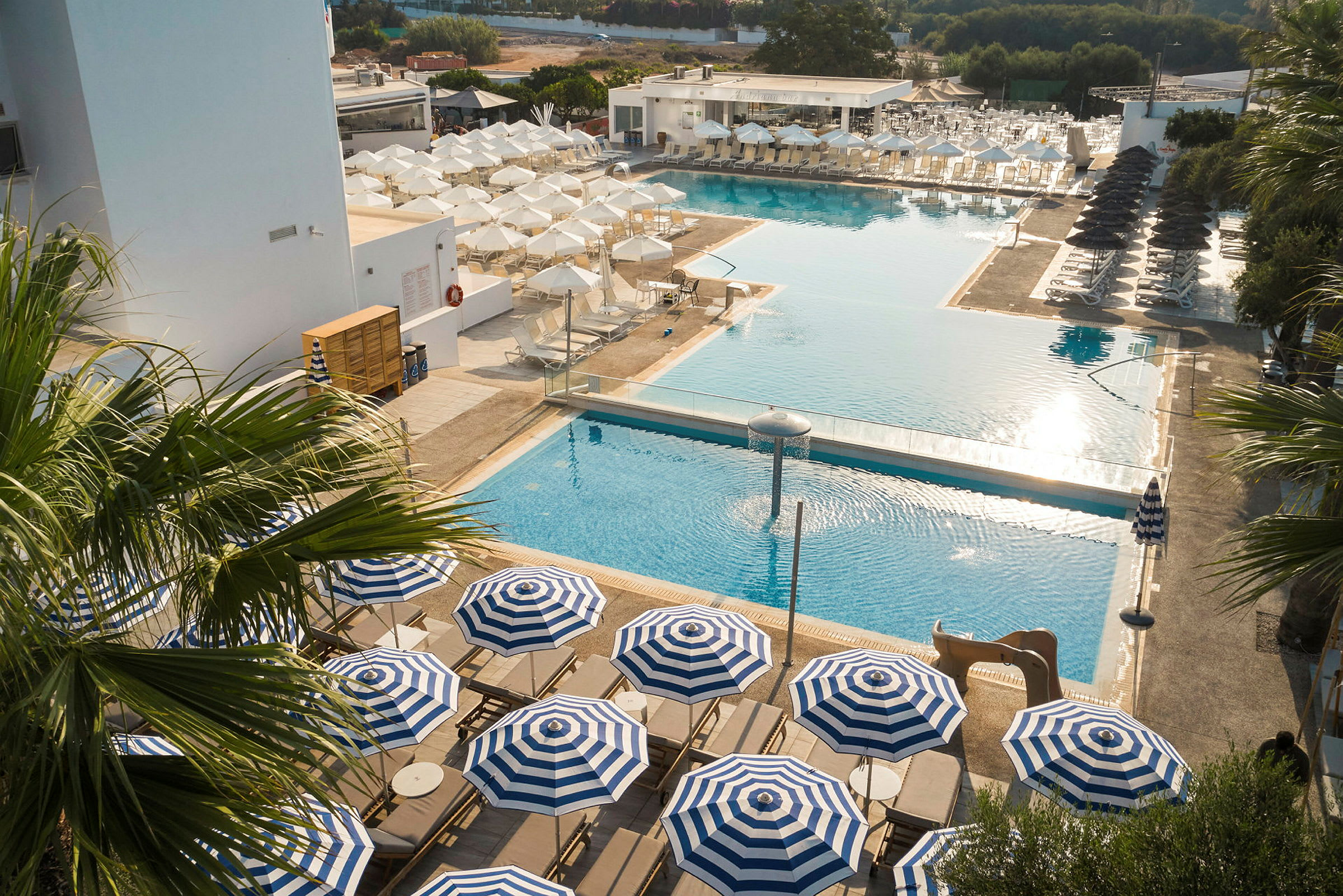En vy över poolområdet på ett hotell med solstolar och blå- och vitrandiga parasoller. (AI-genererad text)