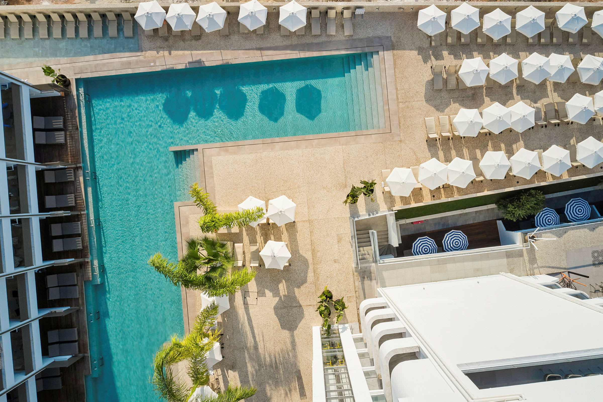 Flygbild över en pool med solstolar och parasoller omkring. (AI-genererad text)