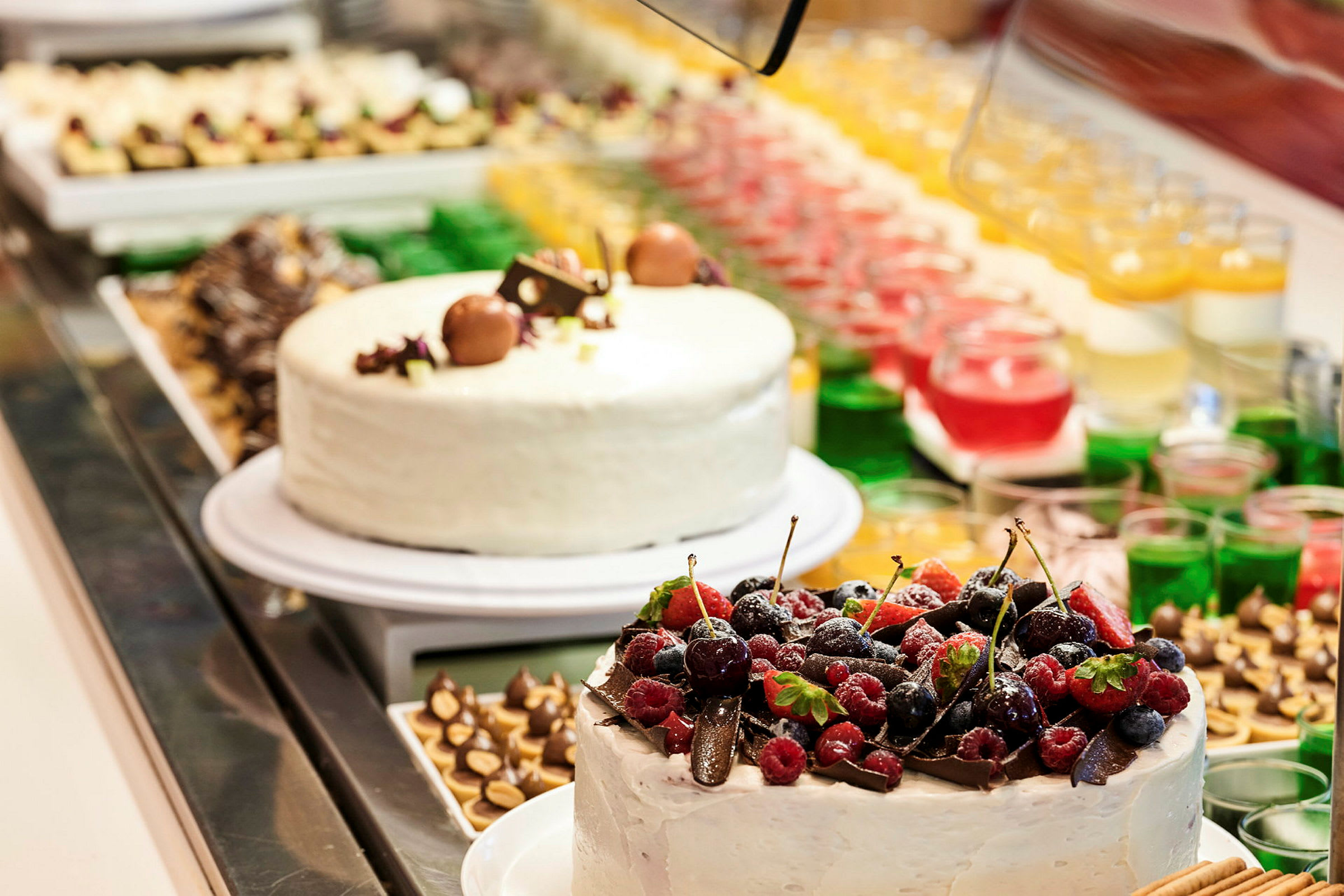 Två dekorerade tårtor på ett buffébord omgivna av andra desserter och små glas med färggranna desserter. (AI-genererad text)