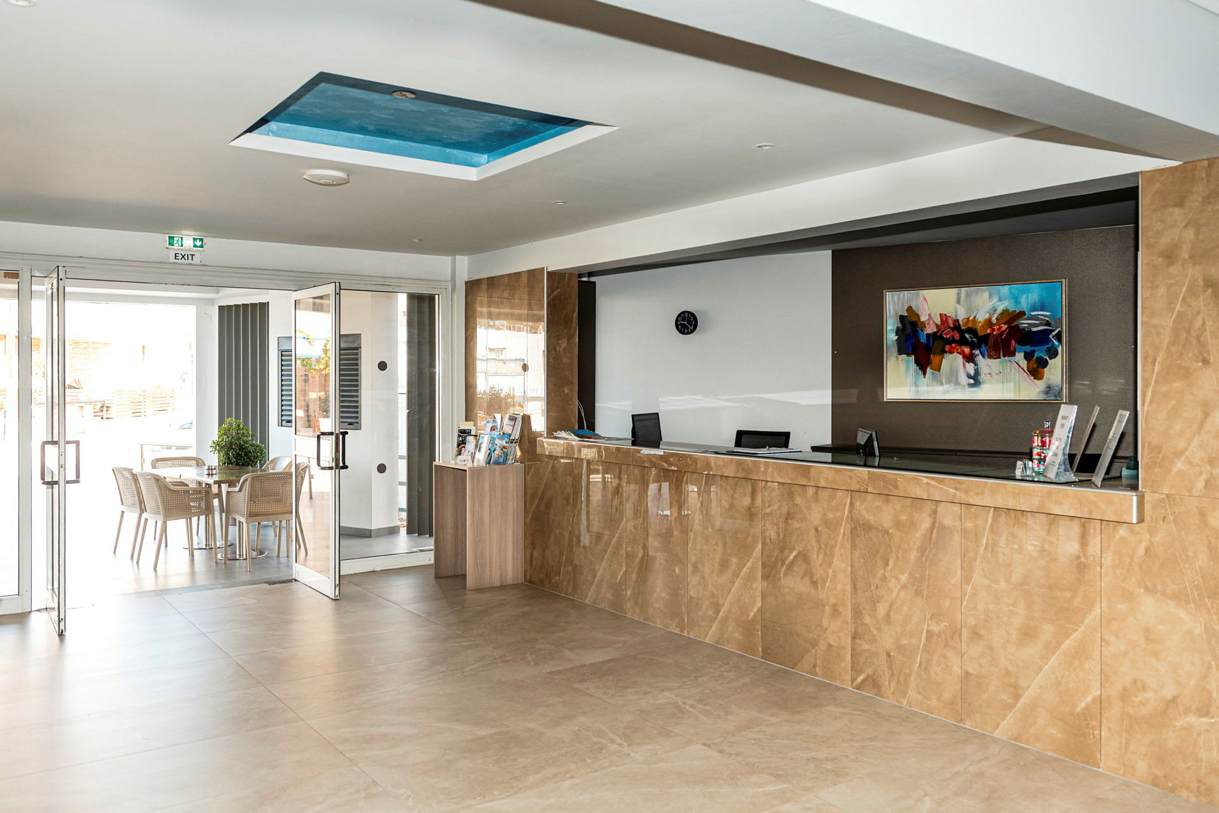 Bild av en hotellreception med en marmorerad disk och en öppning mot en uteplats med sittmöbler. (AI-genererad text)