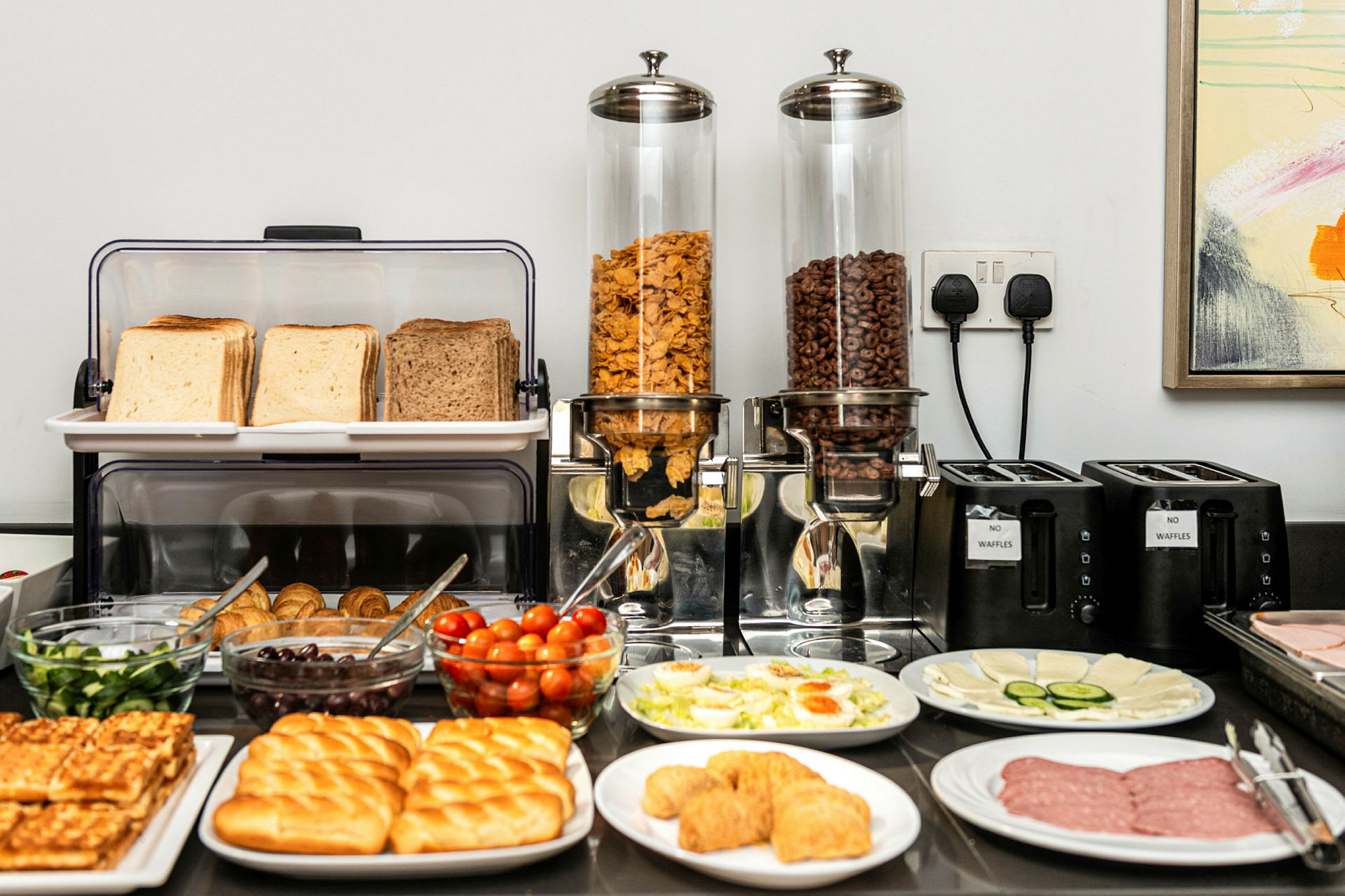 En frukostbuffé med bröd, pålägg, grönsaker och flingor. (AI-genererad text)