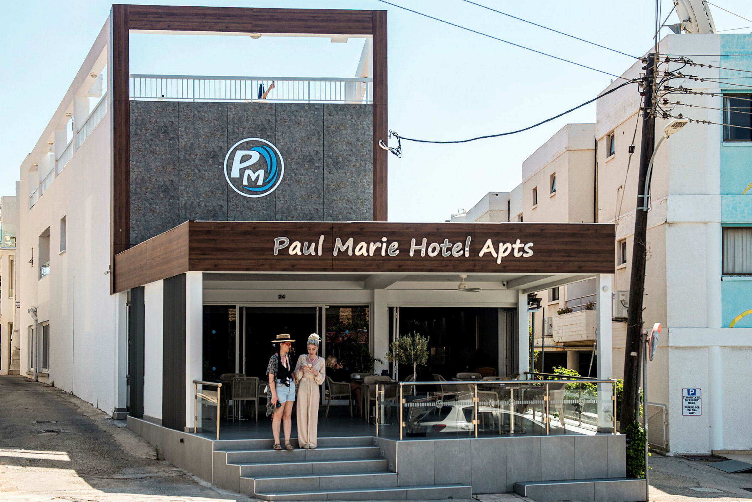 Framsidan av Paul Marie Hotel Apartments med uteservering och entré. (AI-genererad text)