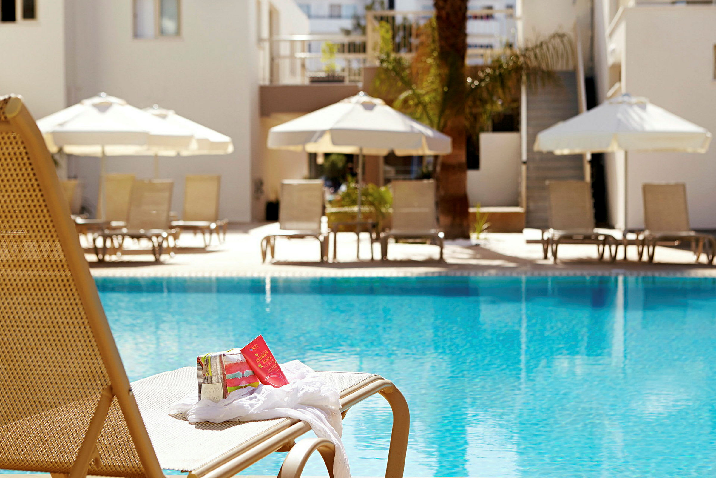 En solstol vid en pool med parasoller och solstolar i bakgrunden. (AI-genererad text)