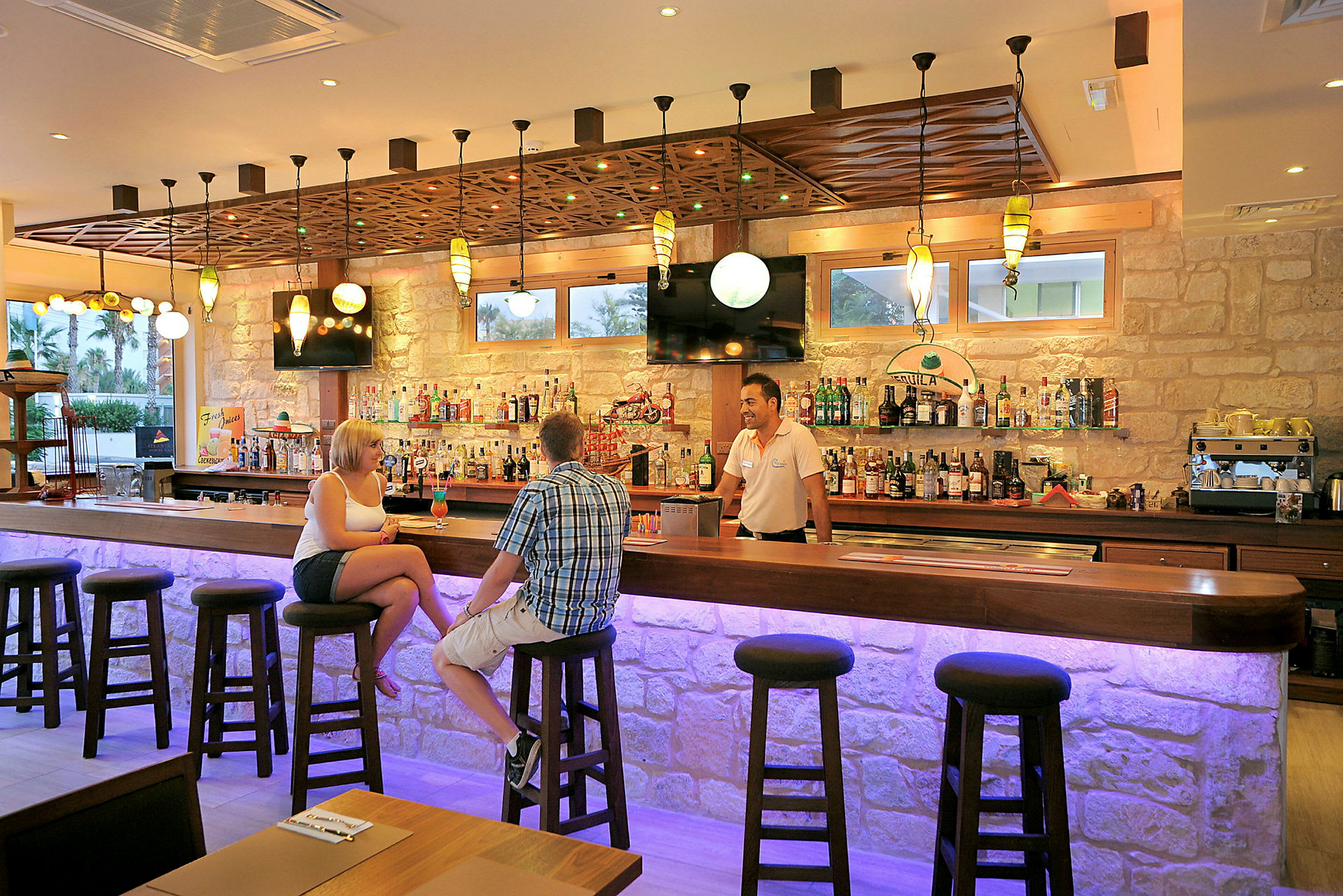 Interiör av en bar med en upplyst bardisk och människor som sitter på barstolar. (AI-genererad text)