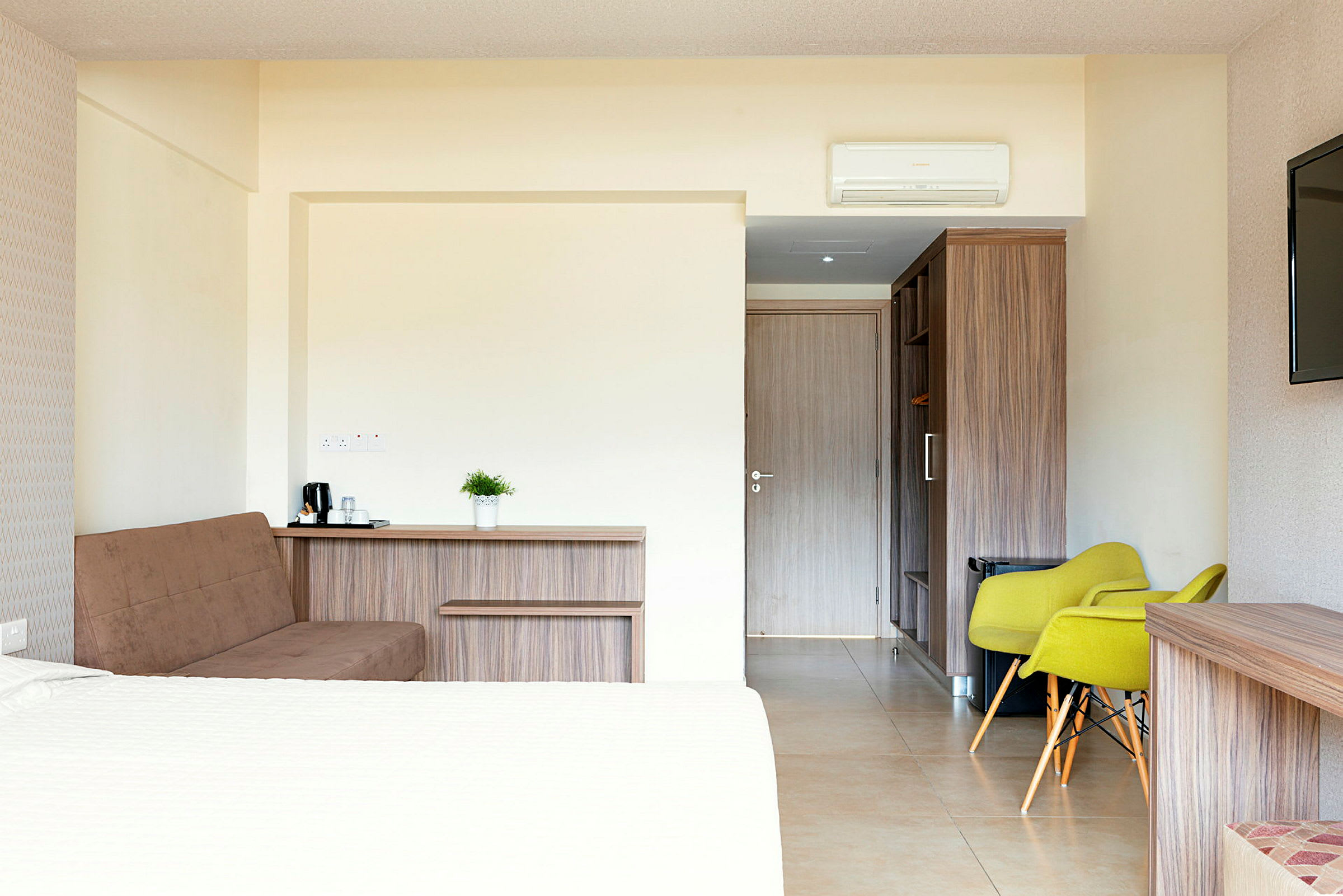 Interiörbild av ett hotellrum med säng, sittplatser och dörr. (AI-genererad text)