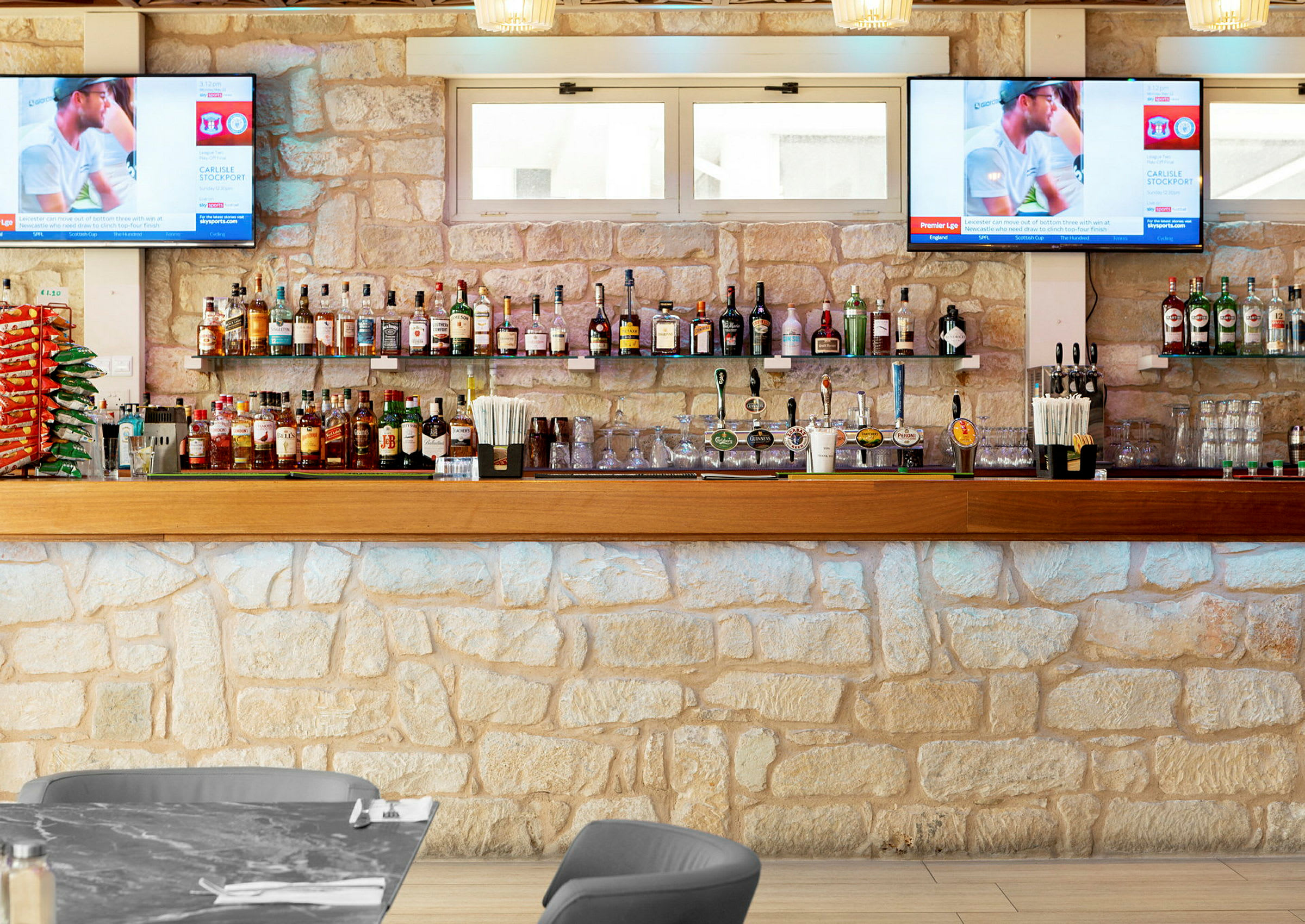Fokus på en bar med stenbeklädd vägg, hyllor med spritflaskor samt ölkranar. (AI-genererad text)