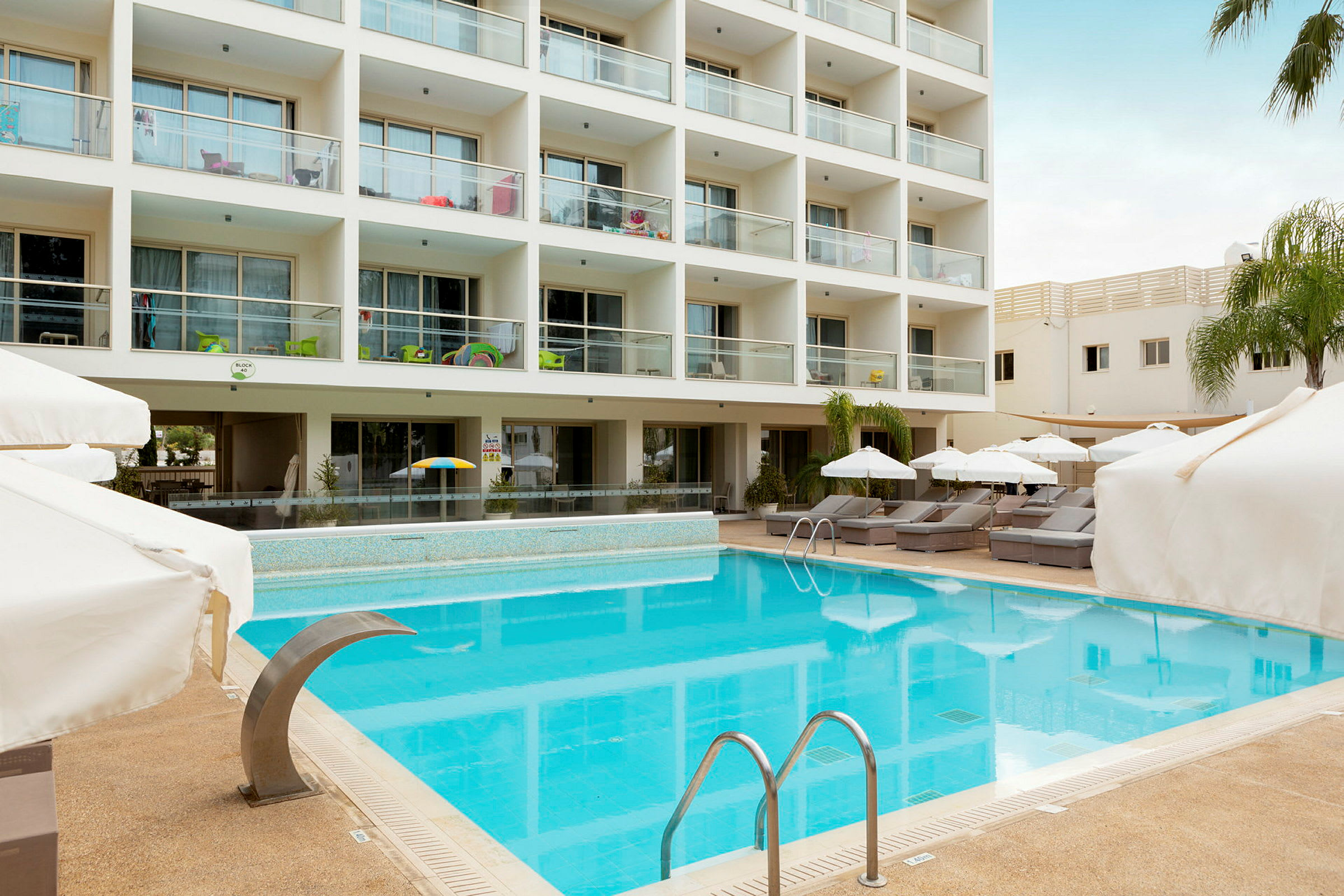 En hotellpool med solsängar och parasoll framför ett flerbostadshus. (AI-genererad text)
