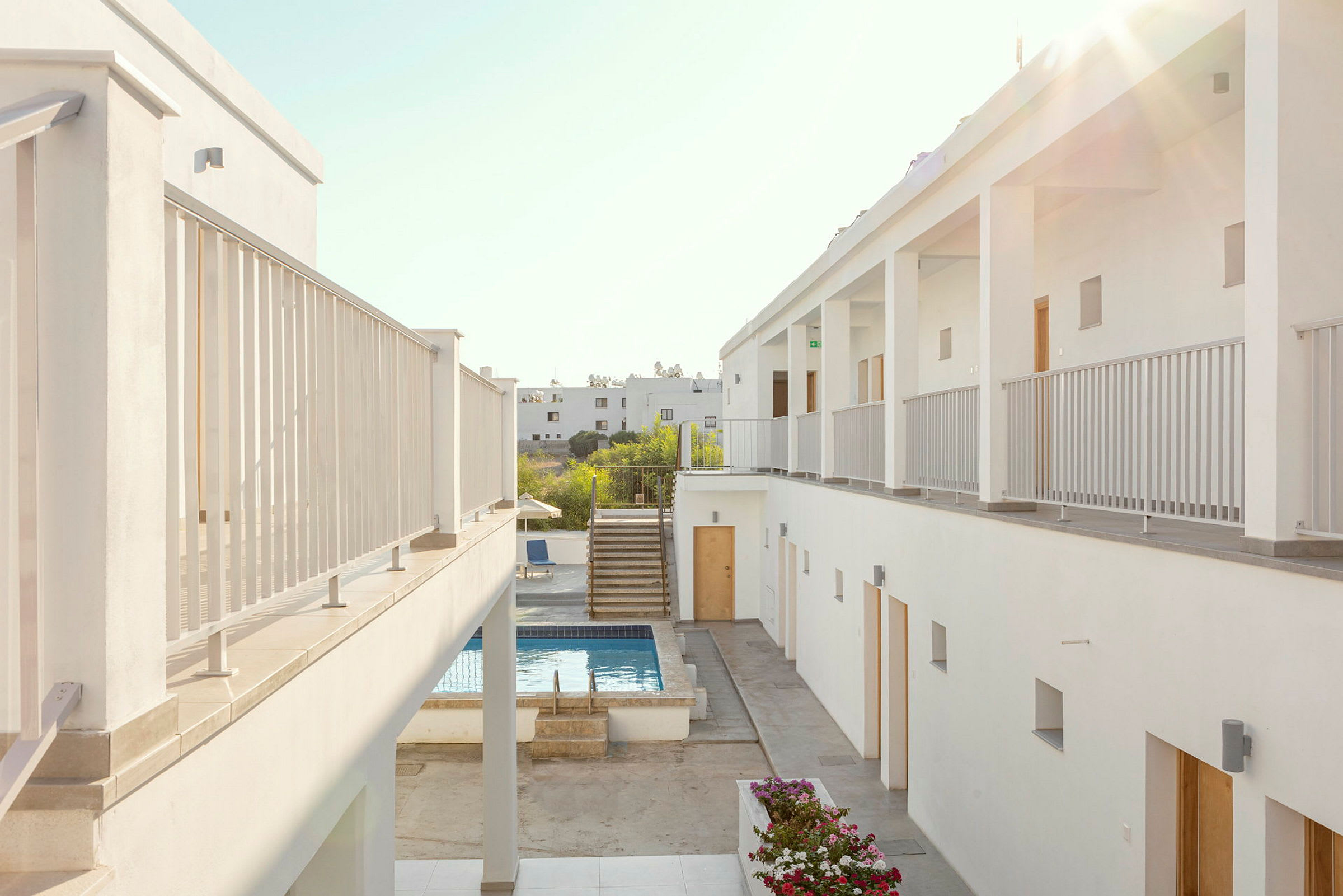 Hotellbyggnader med vita fasader, gångväg och pool i mitten. (AI-genererad text)
