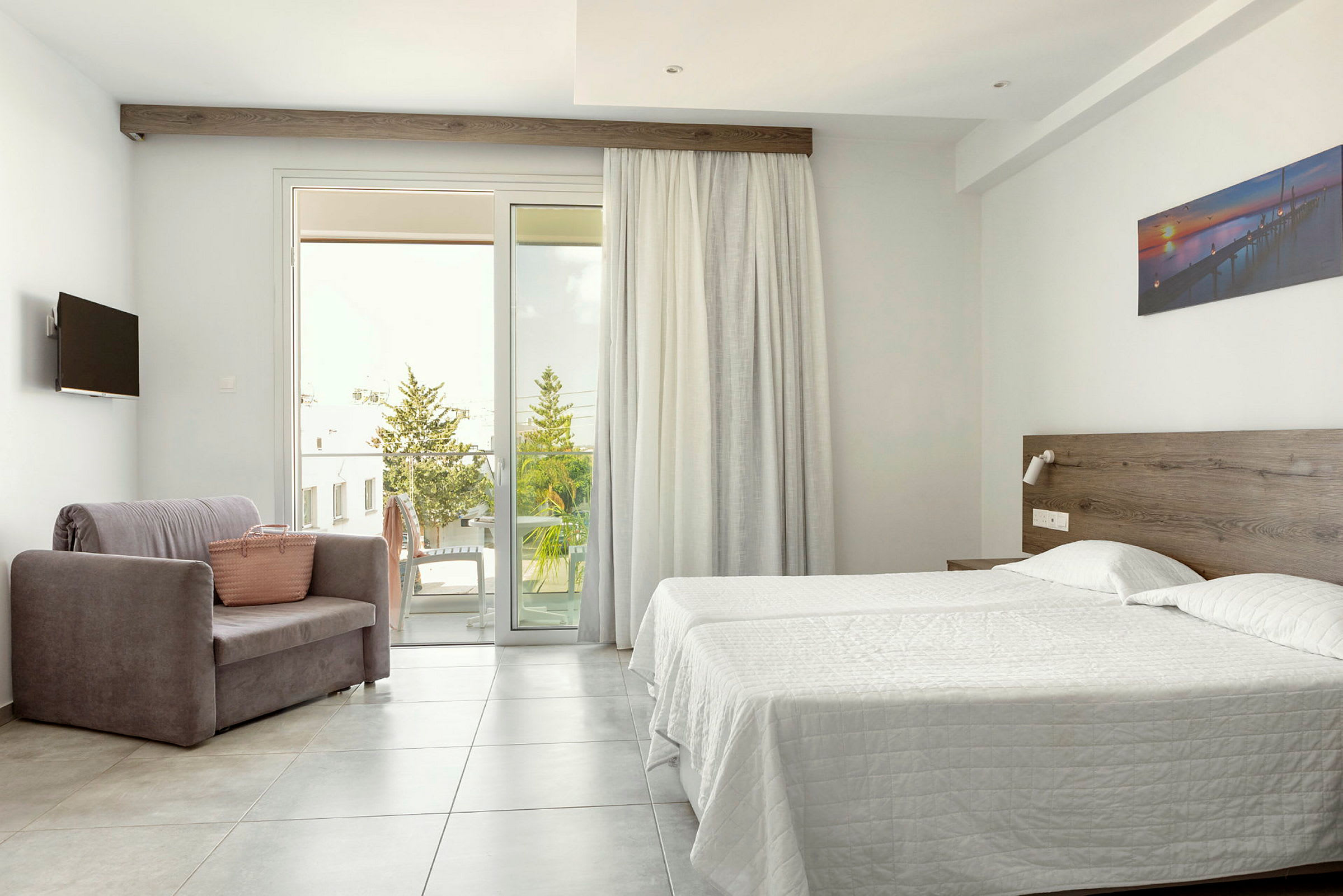Ett hotellrum med två sängar, en fåtölj och en stor glasdörr till balkongen. (AI-genererad text)